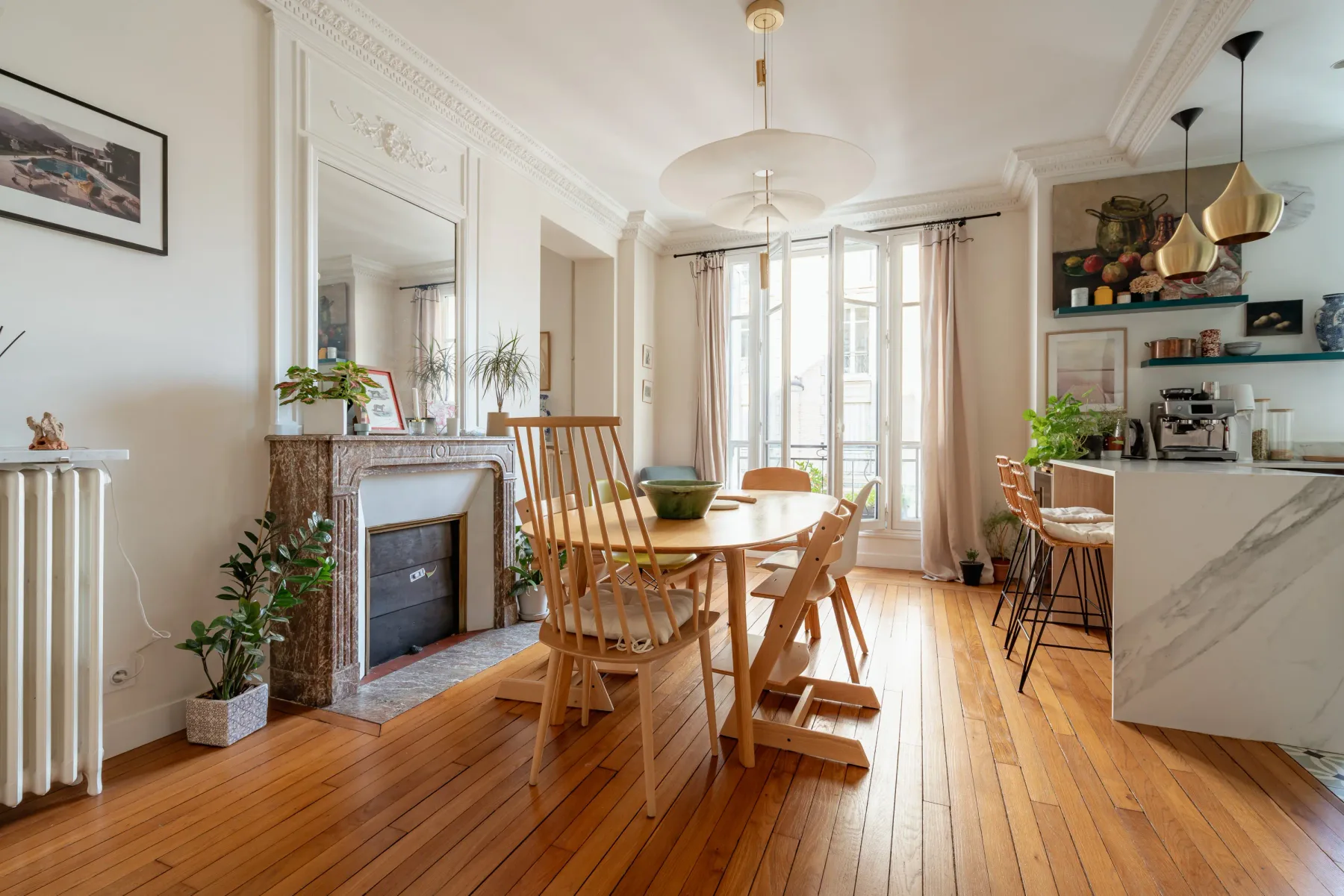 Una luminosa zona de comedor y cocina con una mesa de madera junto a ventanas altas.