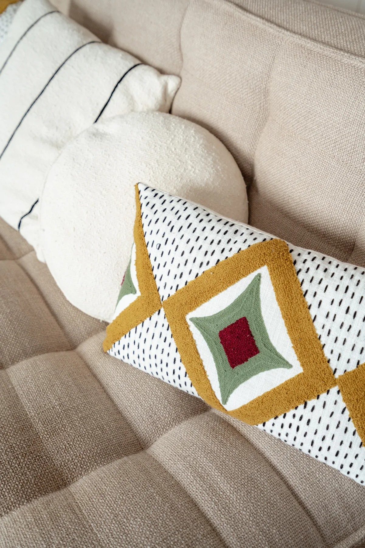 Un sofá beige de sala con varios cojines, incluido uno decorativo estampado.