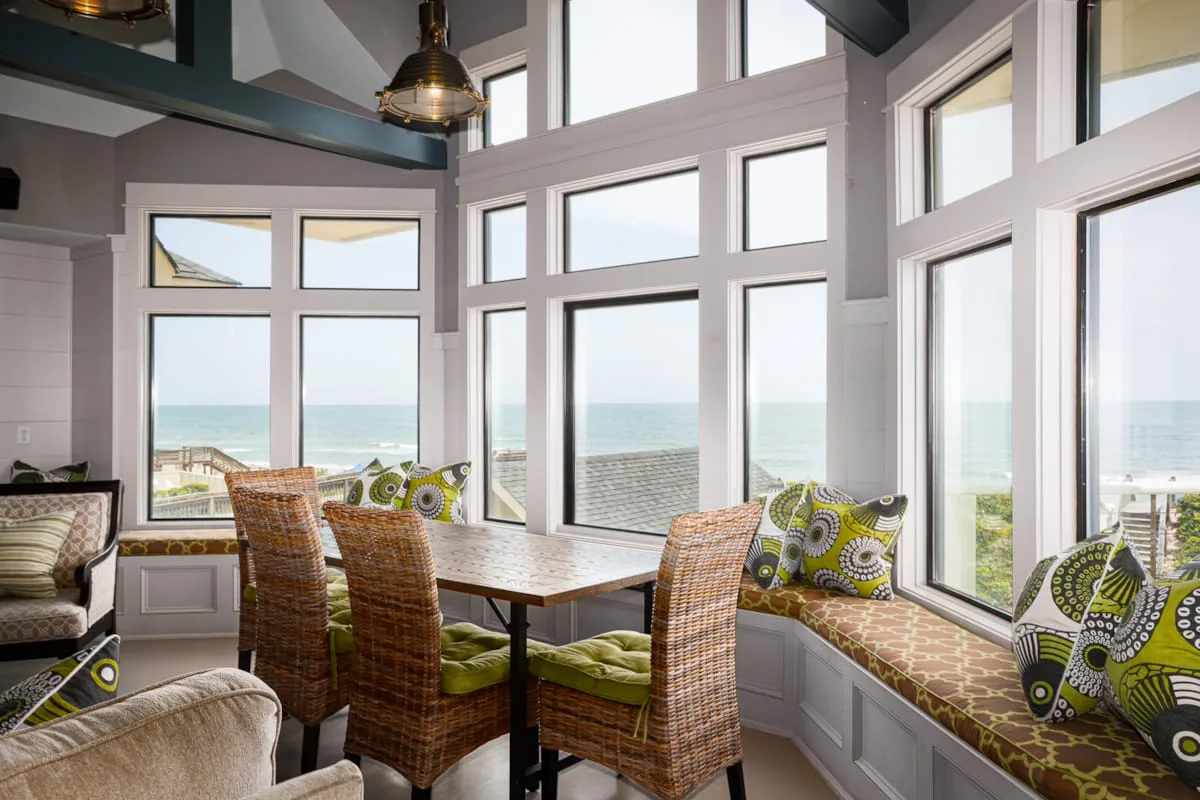 Un luminoso rincón comedor con asientos de mimbre y amplias ventanas con vistas al mar.
