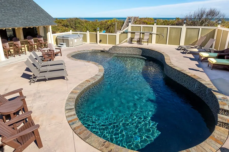 Una piscina curva ocupa un patio soleado al aire libre con asientos alrededor.