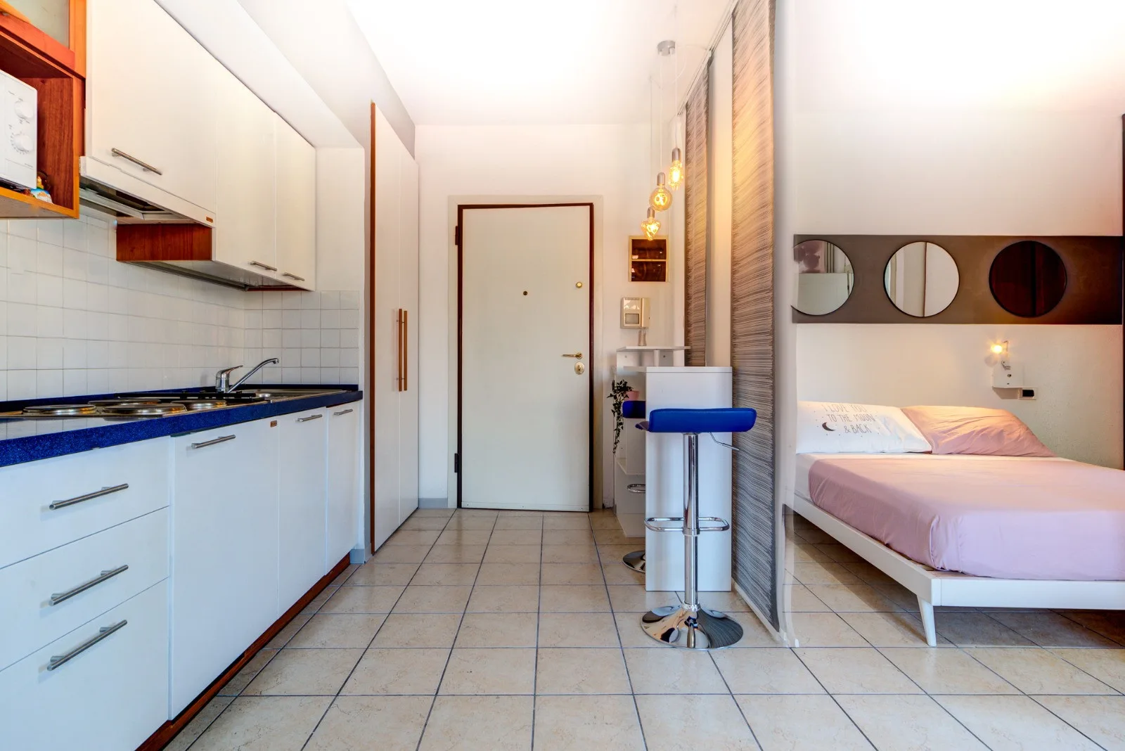 Una cocina compacta da a un dormitorio con una cama y una pequeña barra.