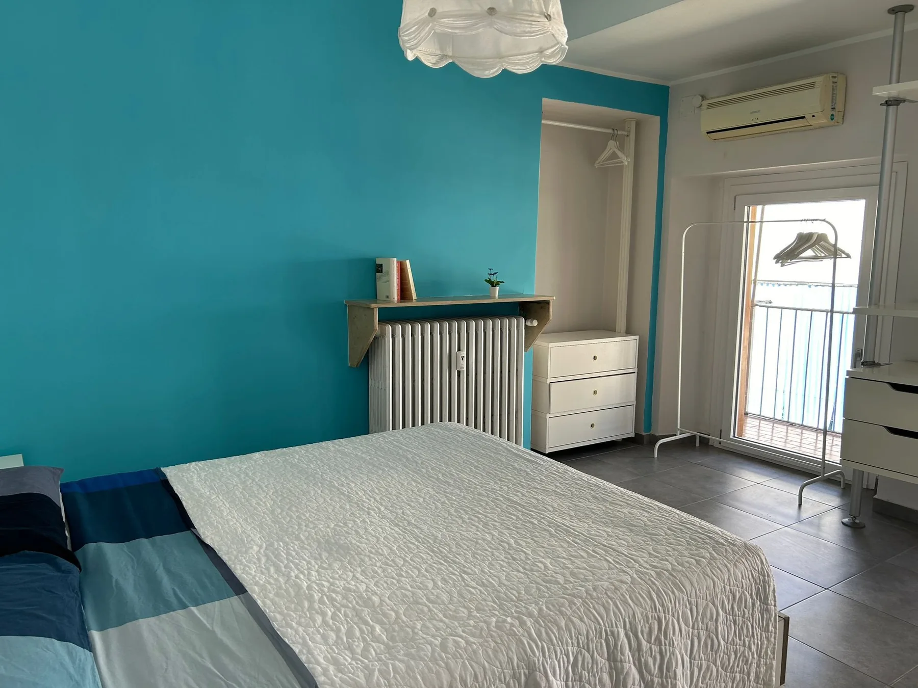 Un dormitorio con una cama, una pared turquesa y una puerta acristalada luminosa.