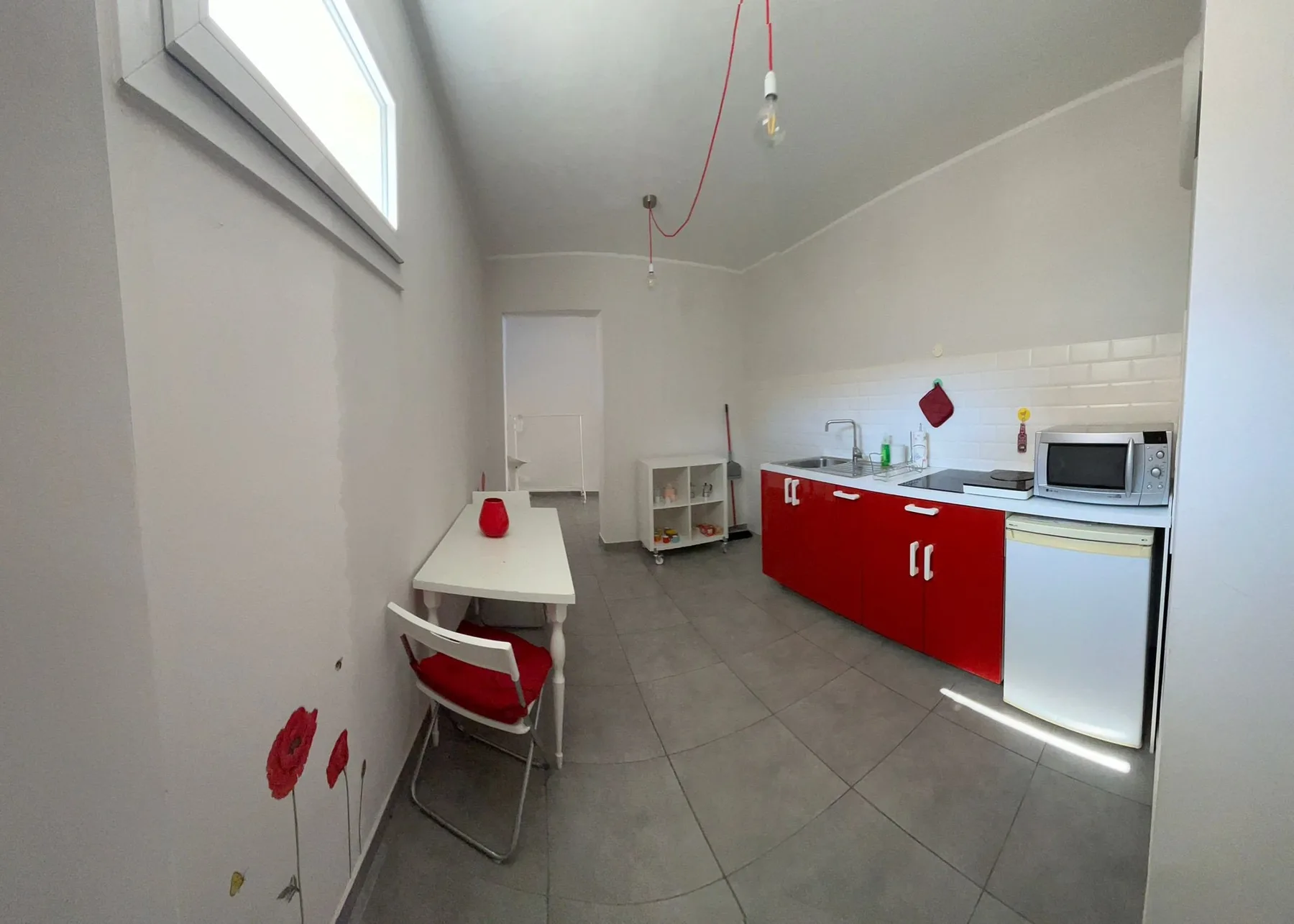 Una cocina compacta con armarios rojos, una encimera y una mesa pequeña.