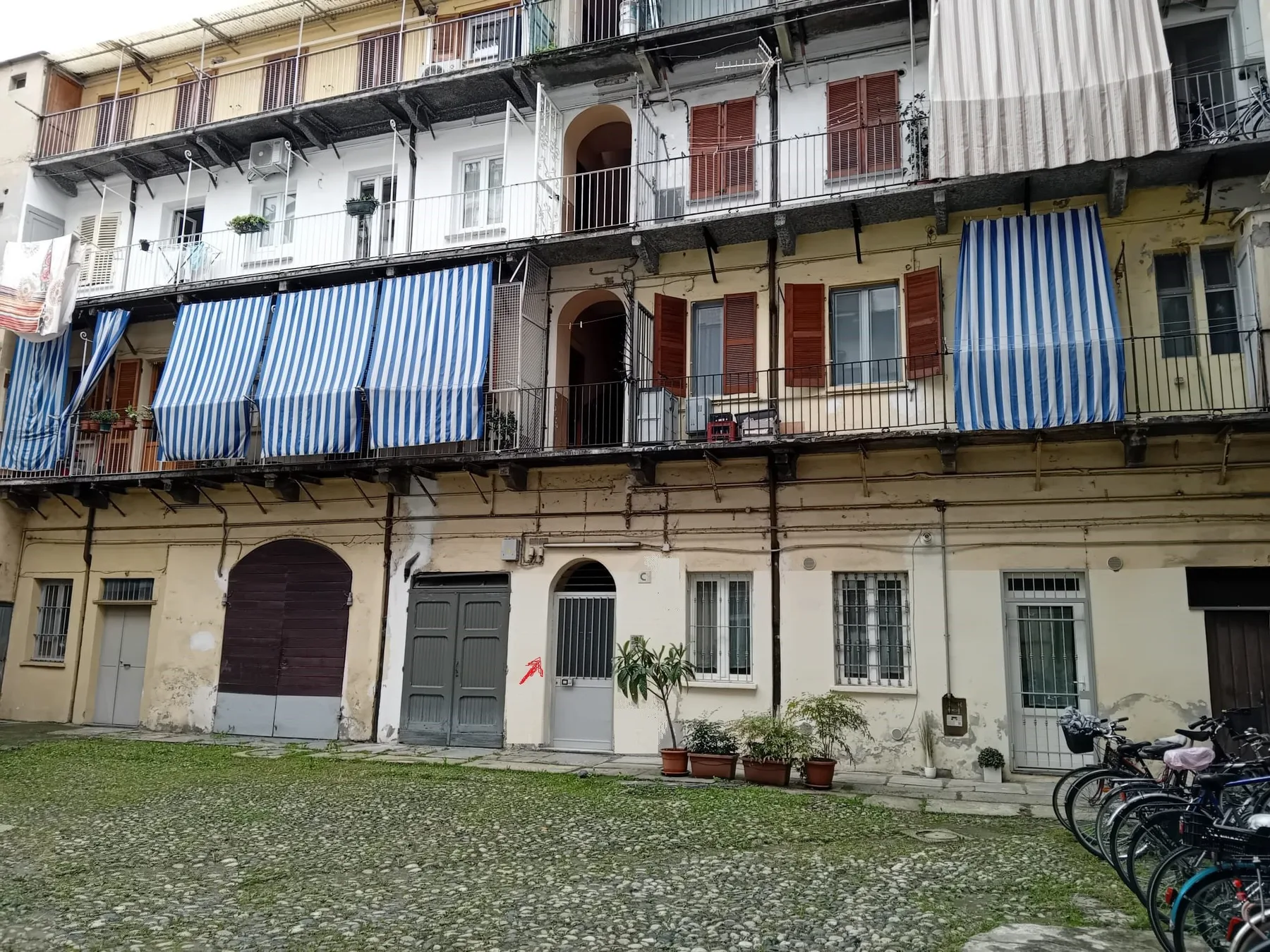 Un edificio de apartamentos desgastado da a un patio empedrado, con toldos a rayas en los balcones.