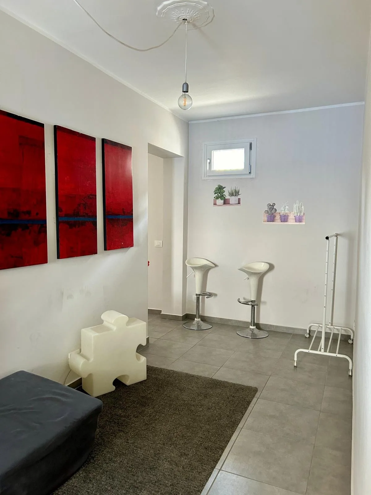 Una habitación luminosa con dos taburetes, arte mural y una ventana pequeña.