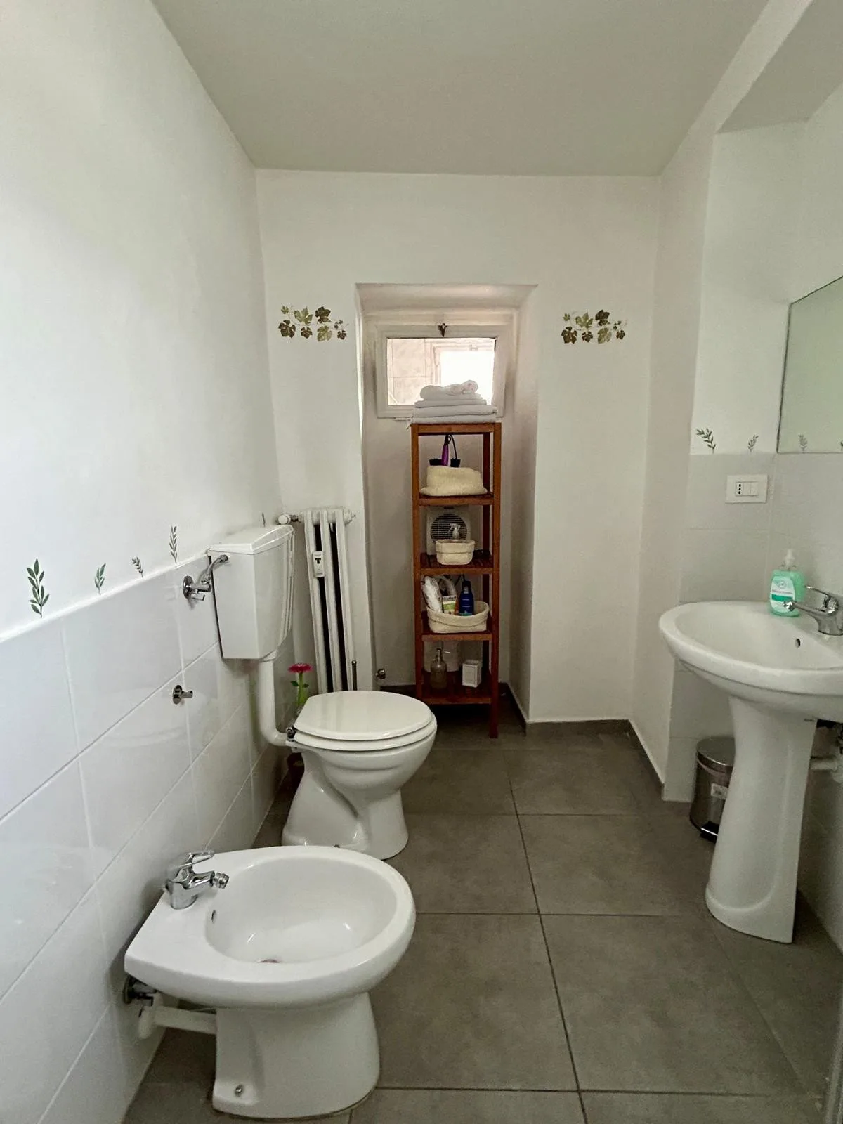 Un baño alicatado con inodoro, bidé, lavabo con pedestal y estantería.