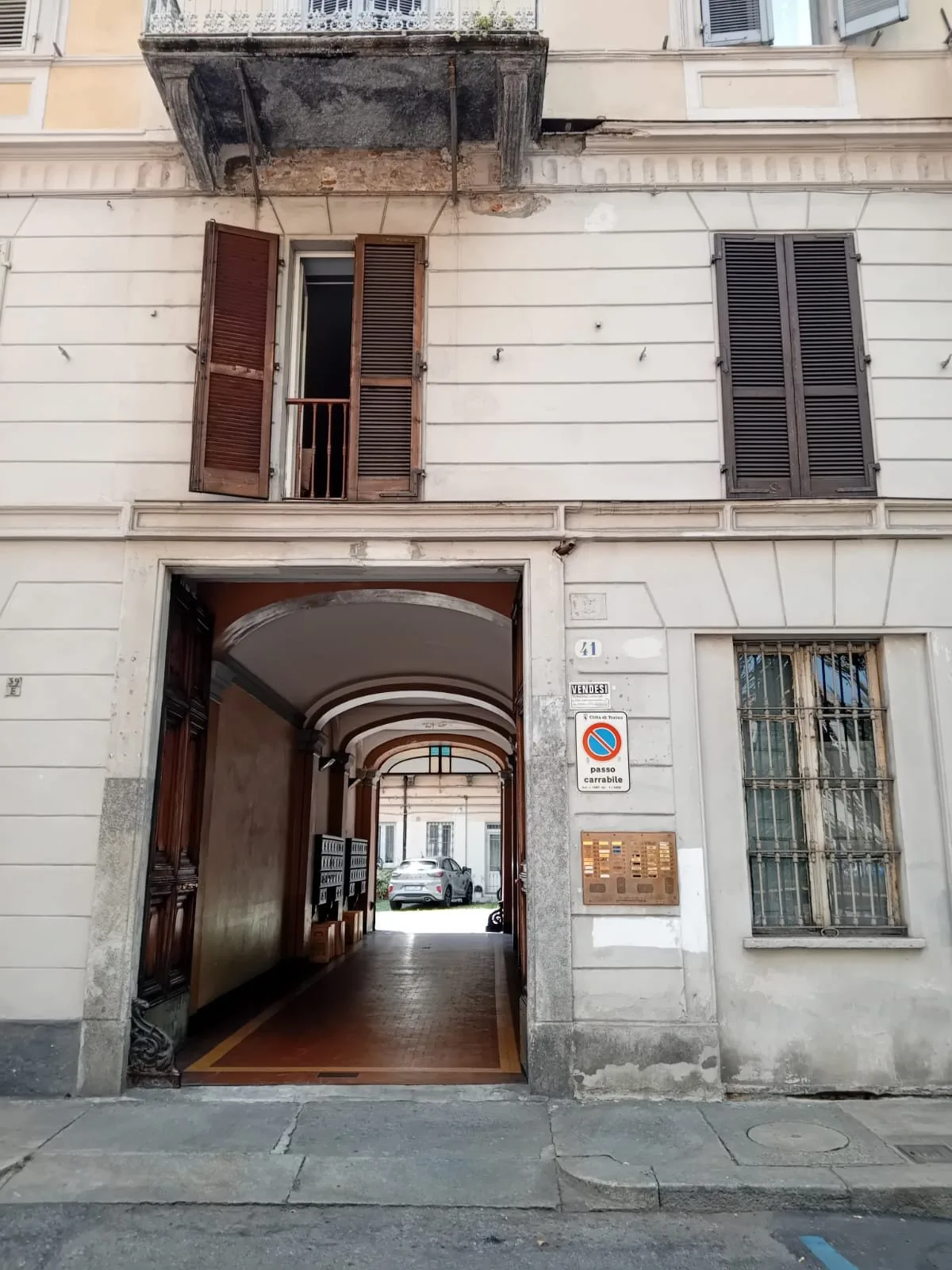 La entrada de un edificio da a un pasaje cubierto, con un automóvil visible al fondo.
