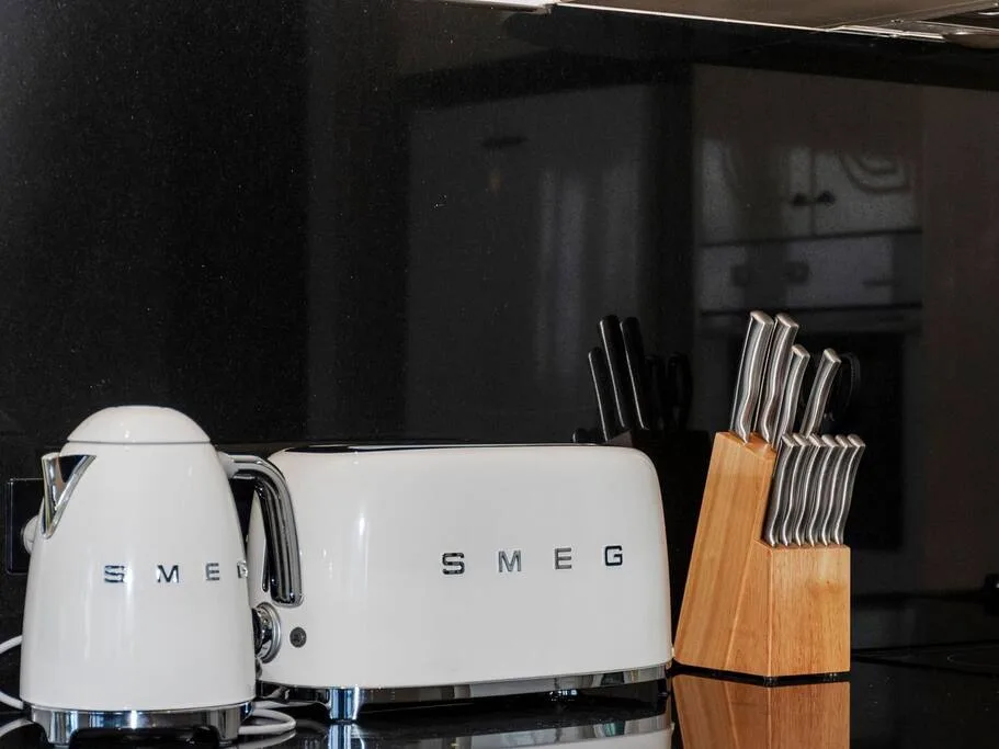 A kitchen counter displays a white kettle, toaster, and wooden knife block.