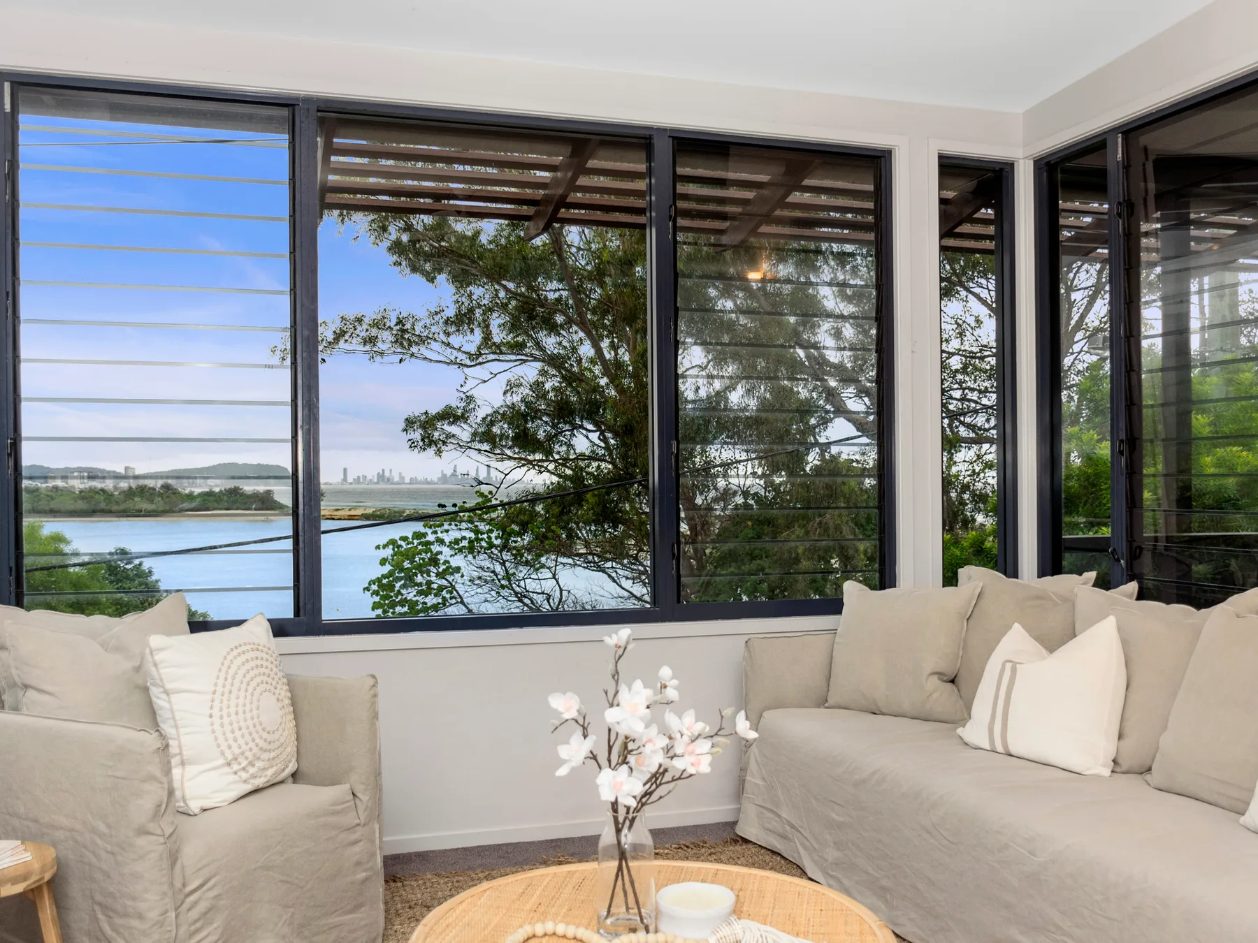 A bright living room with pale seating and broad windows overlooking the water.