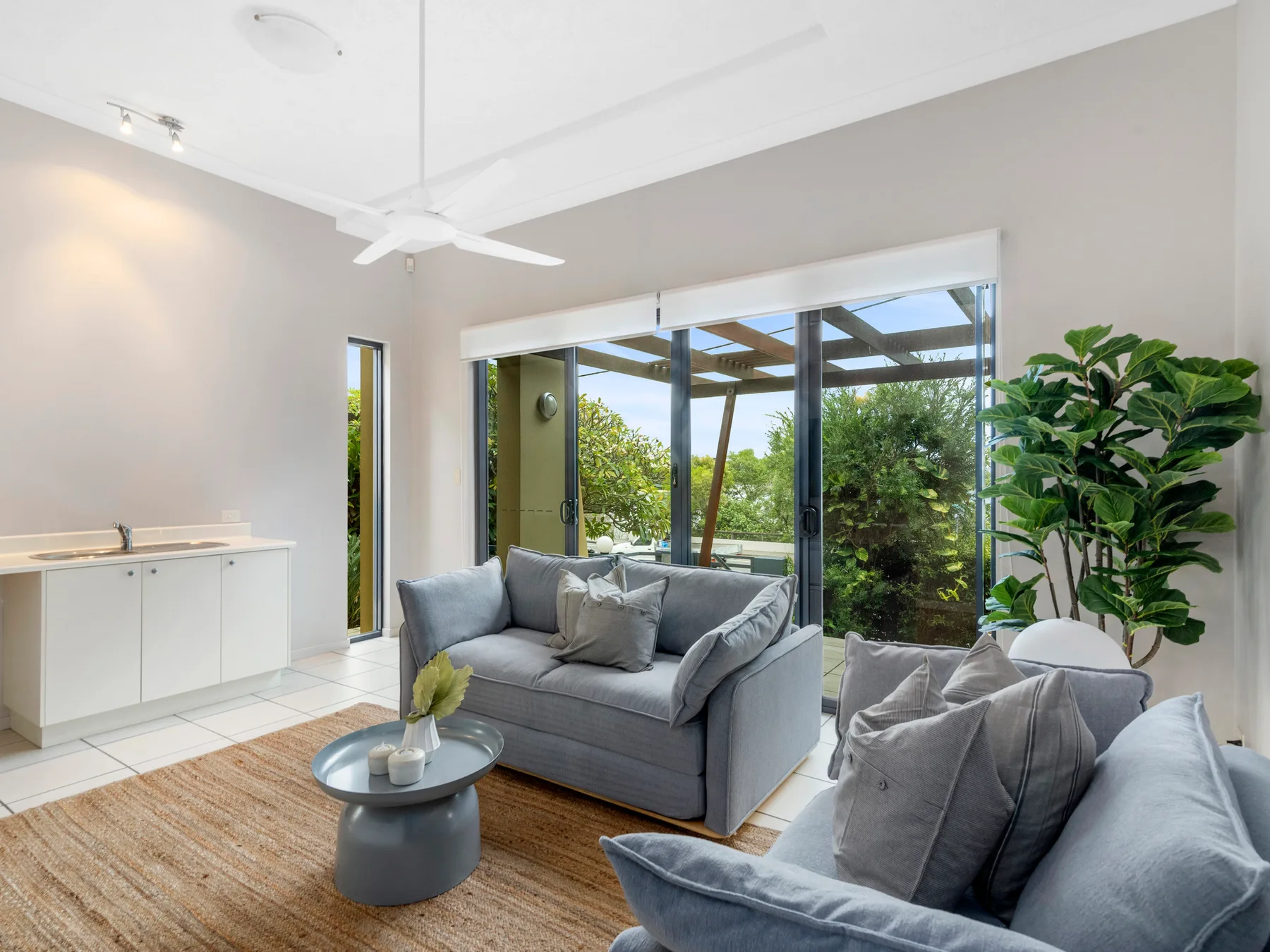 A bright living room with gray seating beside large glass doors and greenery.