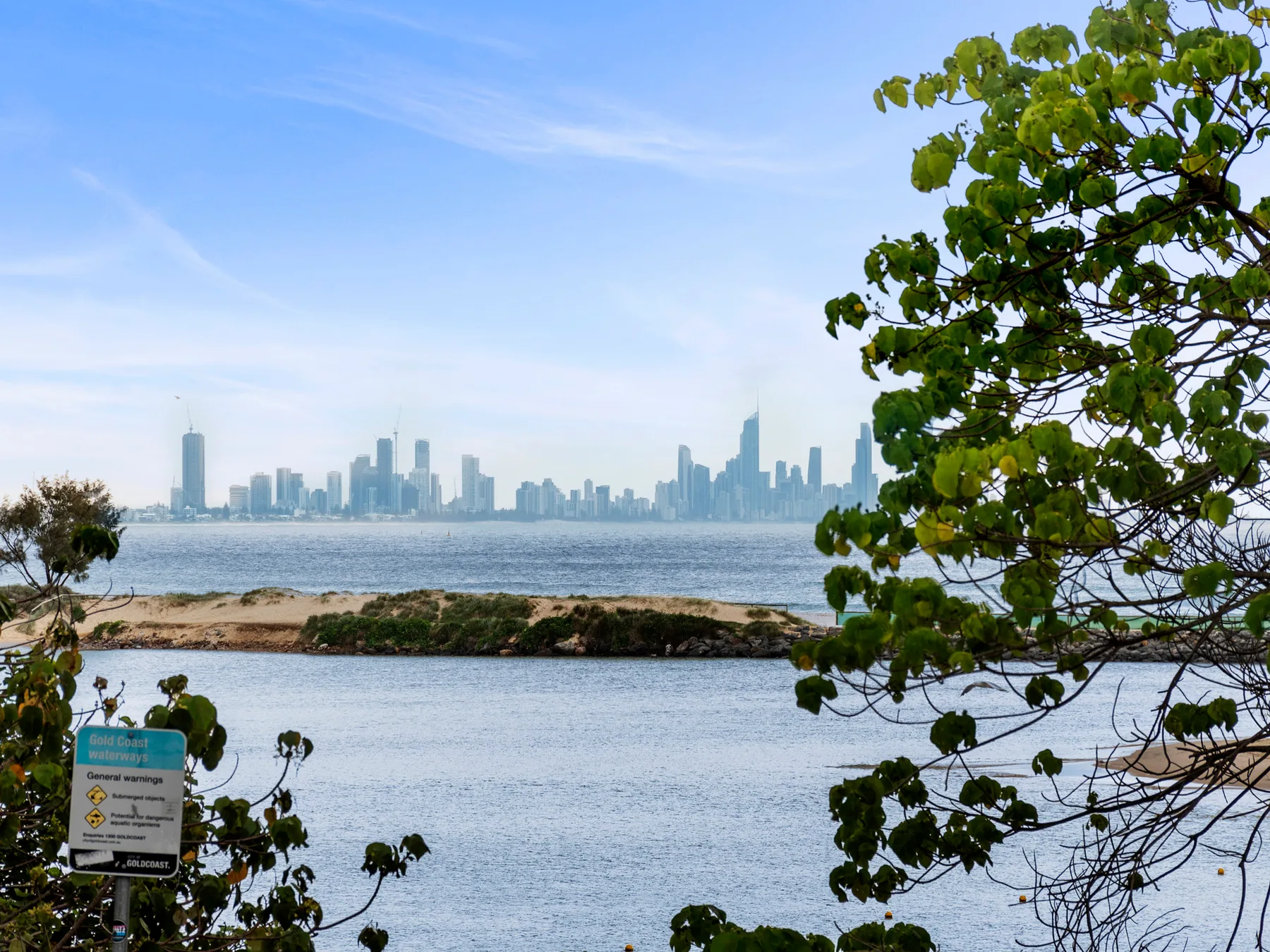 A waterfront view shows a distant city skyline across the water, framed by trees.