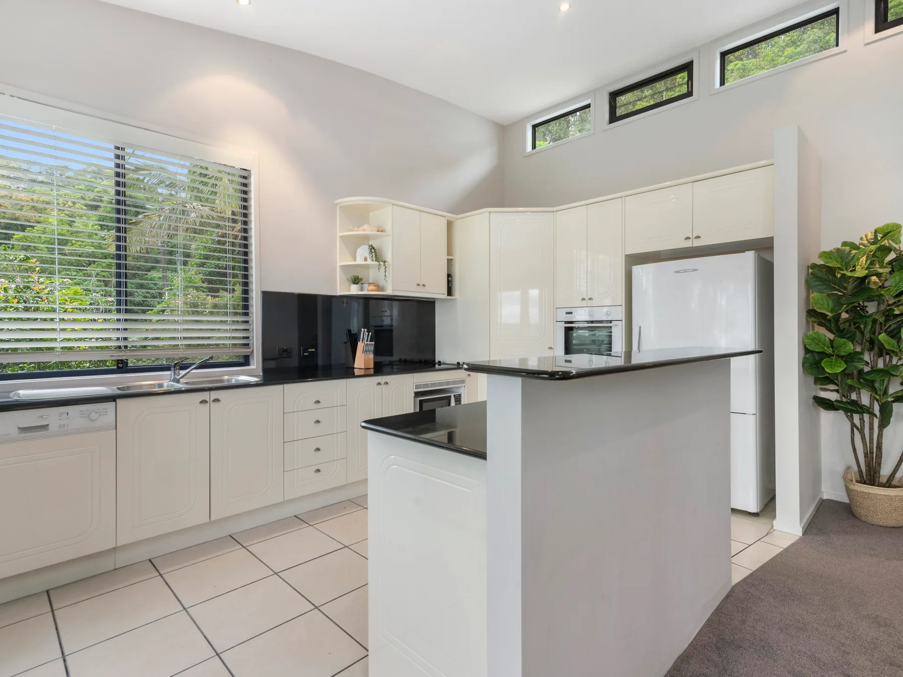 A bright kitchen with white cabinetry, dark countertops, and a central island.