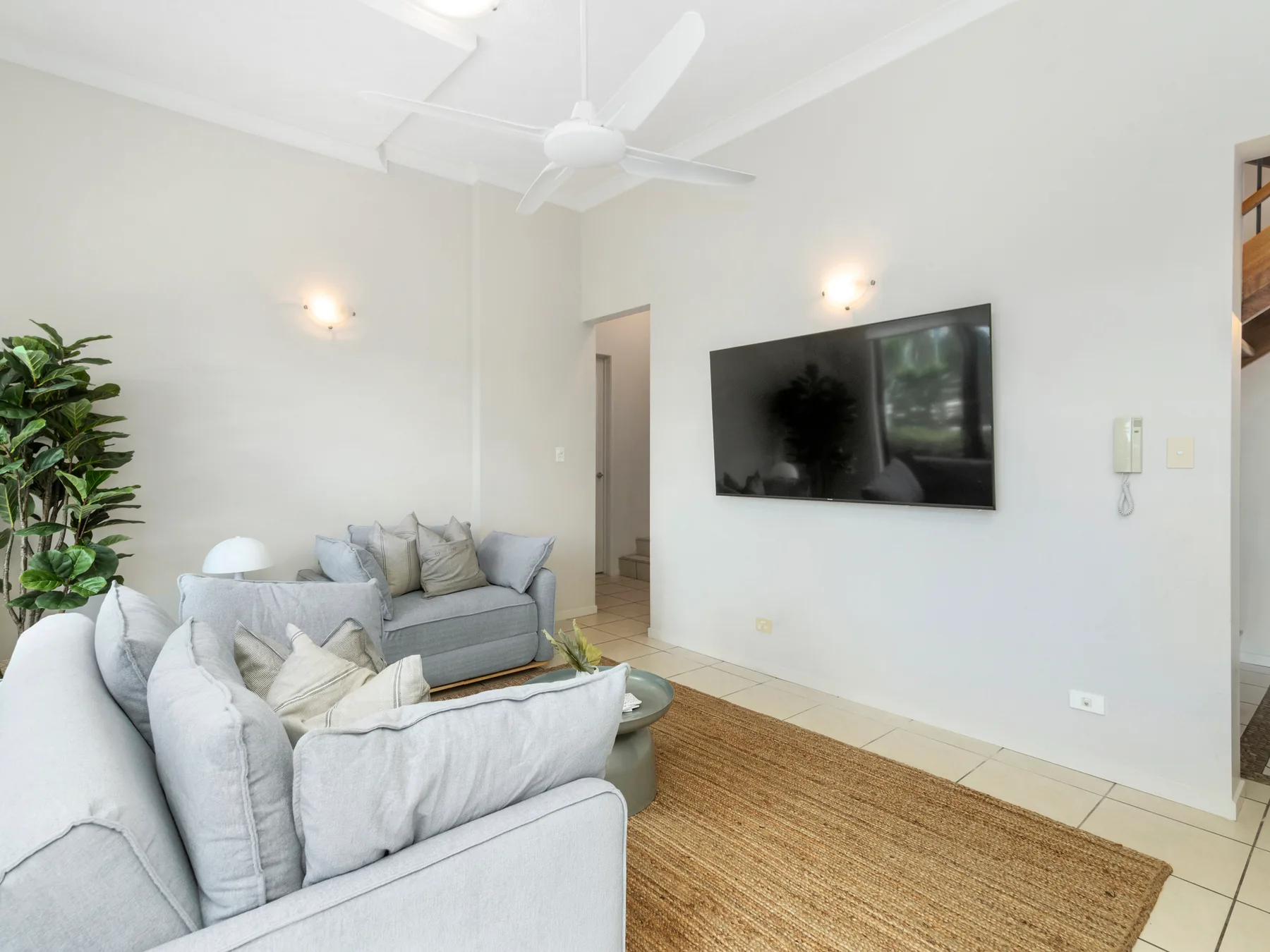 A bright living room with light-colored seating and a wall-mounted television.