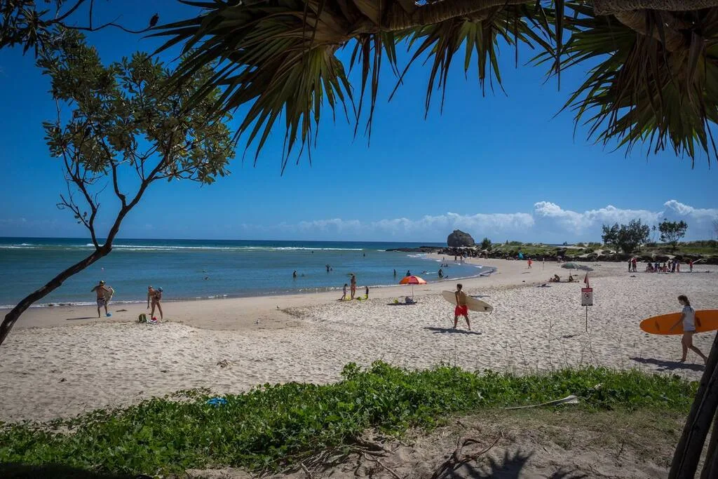 A sandy beach curves alongside calm blue water beneath a clear sky.
