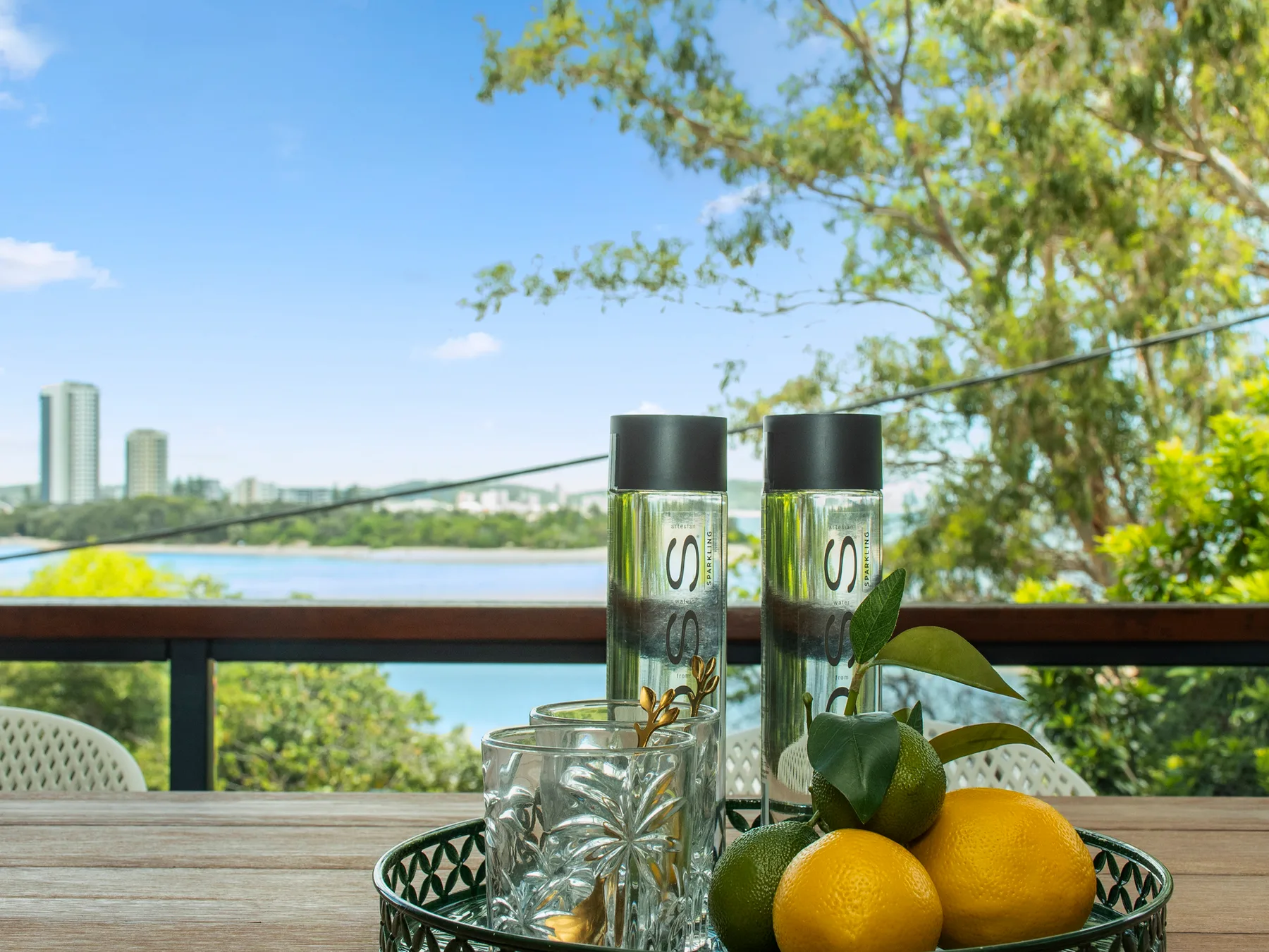 Outdoor dining table with citrus fruit and glass containers overlooking a leafy landscape.