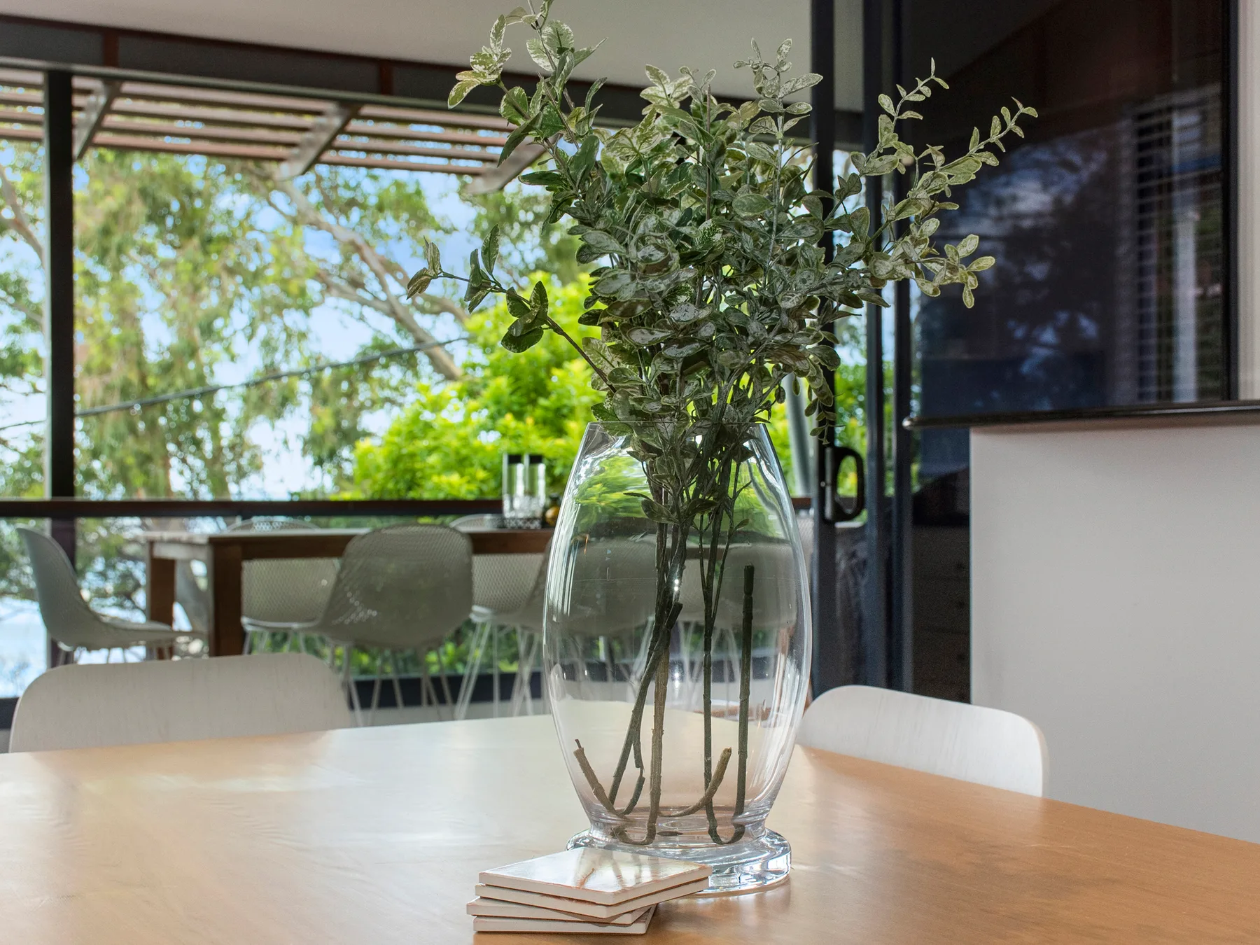 A dining area with a glass vase of leafy branches on the table.