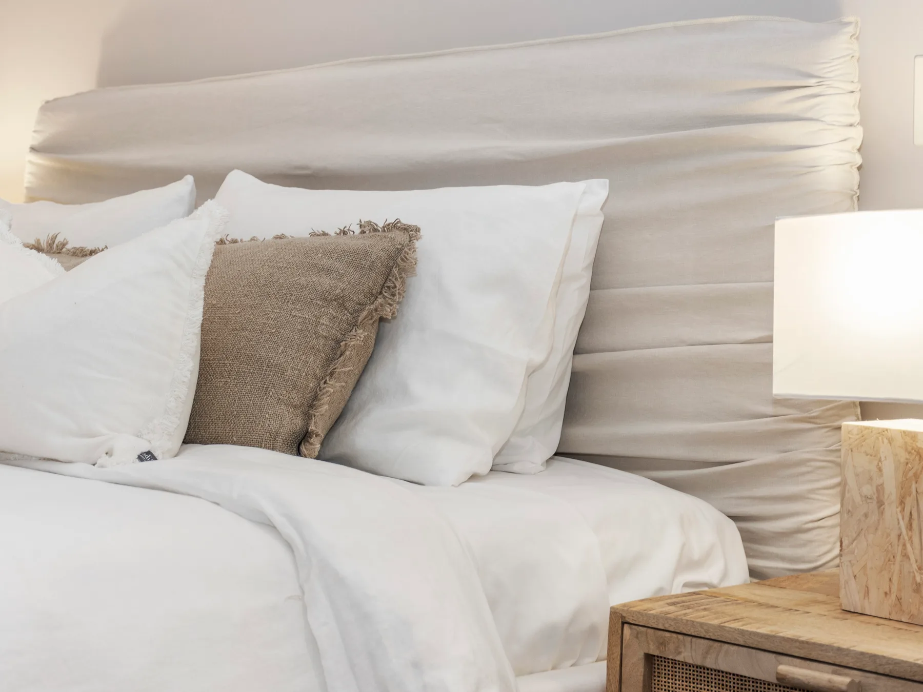 A bedroom with white bedding and neutral accent pillows.