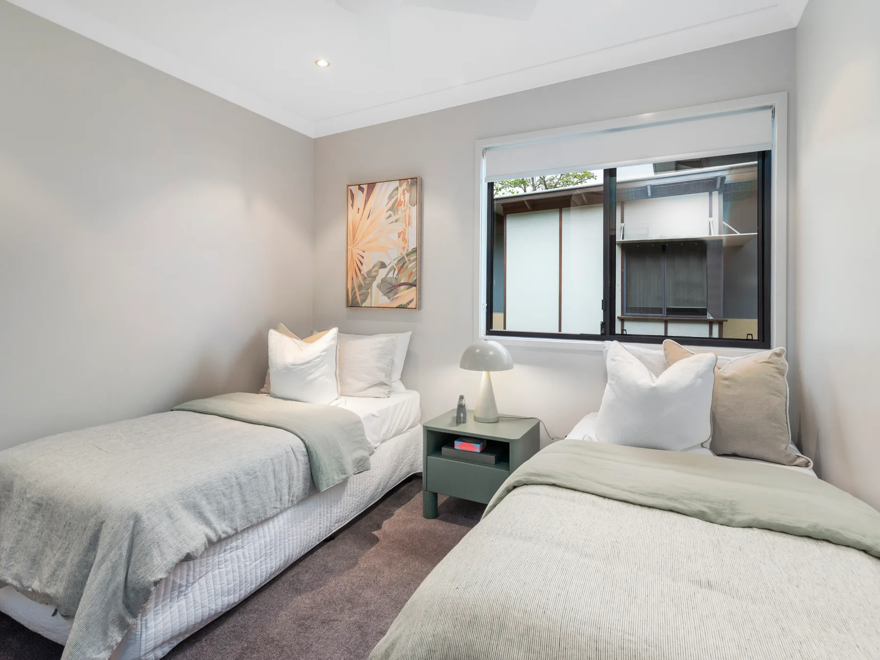 A bedroom with two beds, a bedside table, and a window.