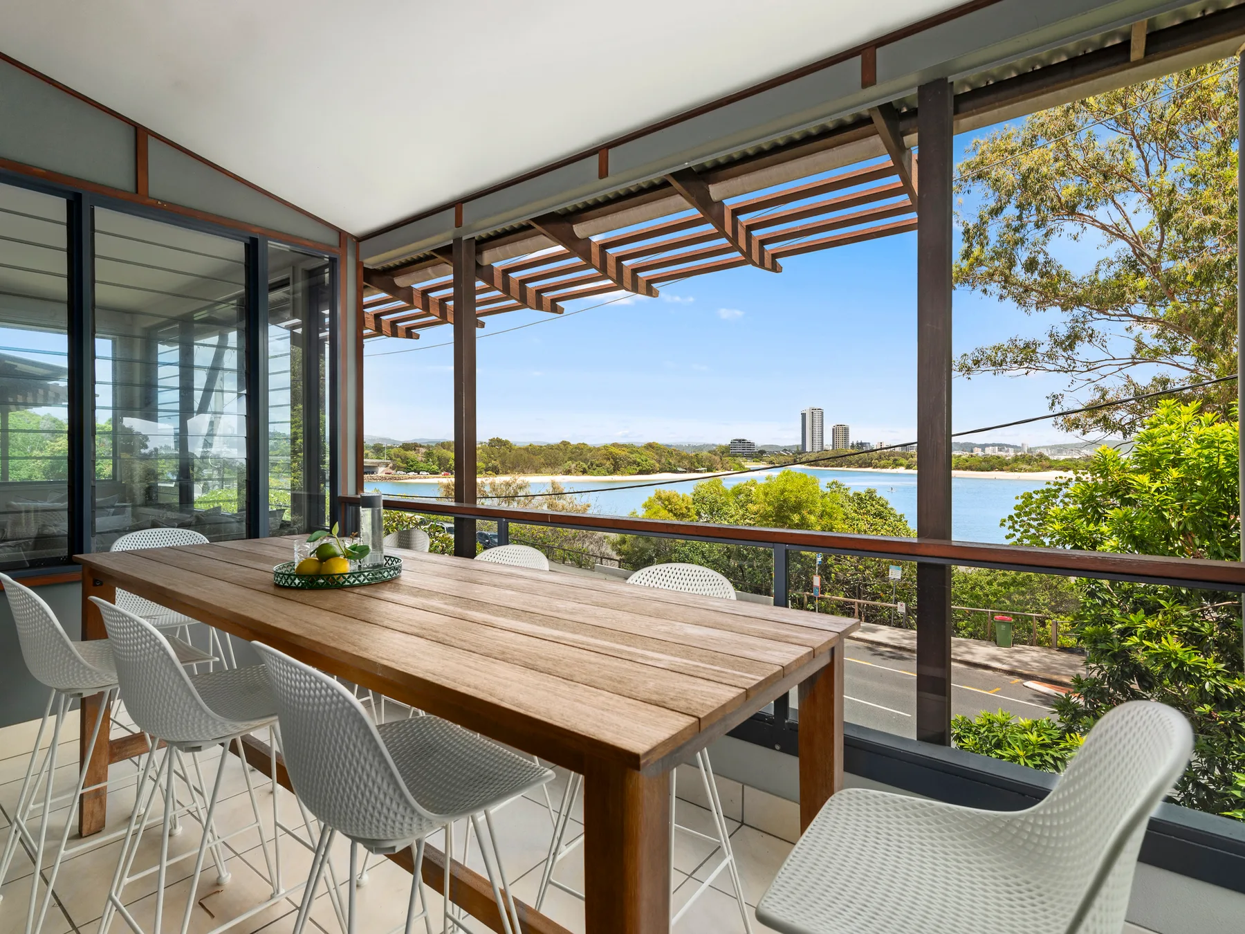 An outdoor dining area overlooks the water beneath a timber pergola.