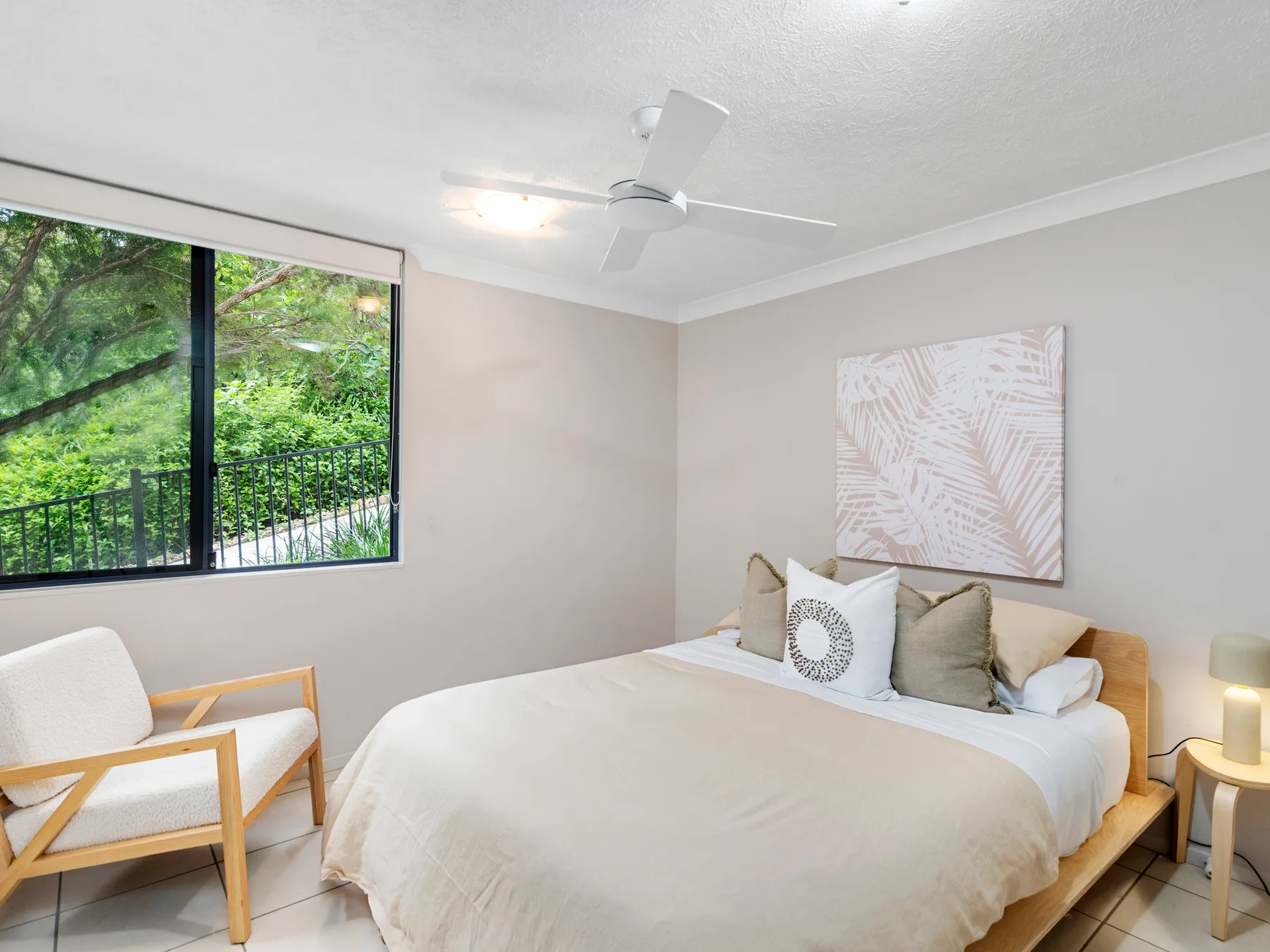 A bright bedroom with a bed beside a large window overlooking greenery.