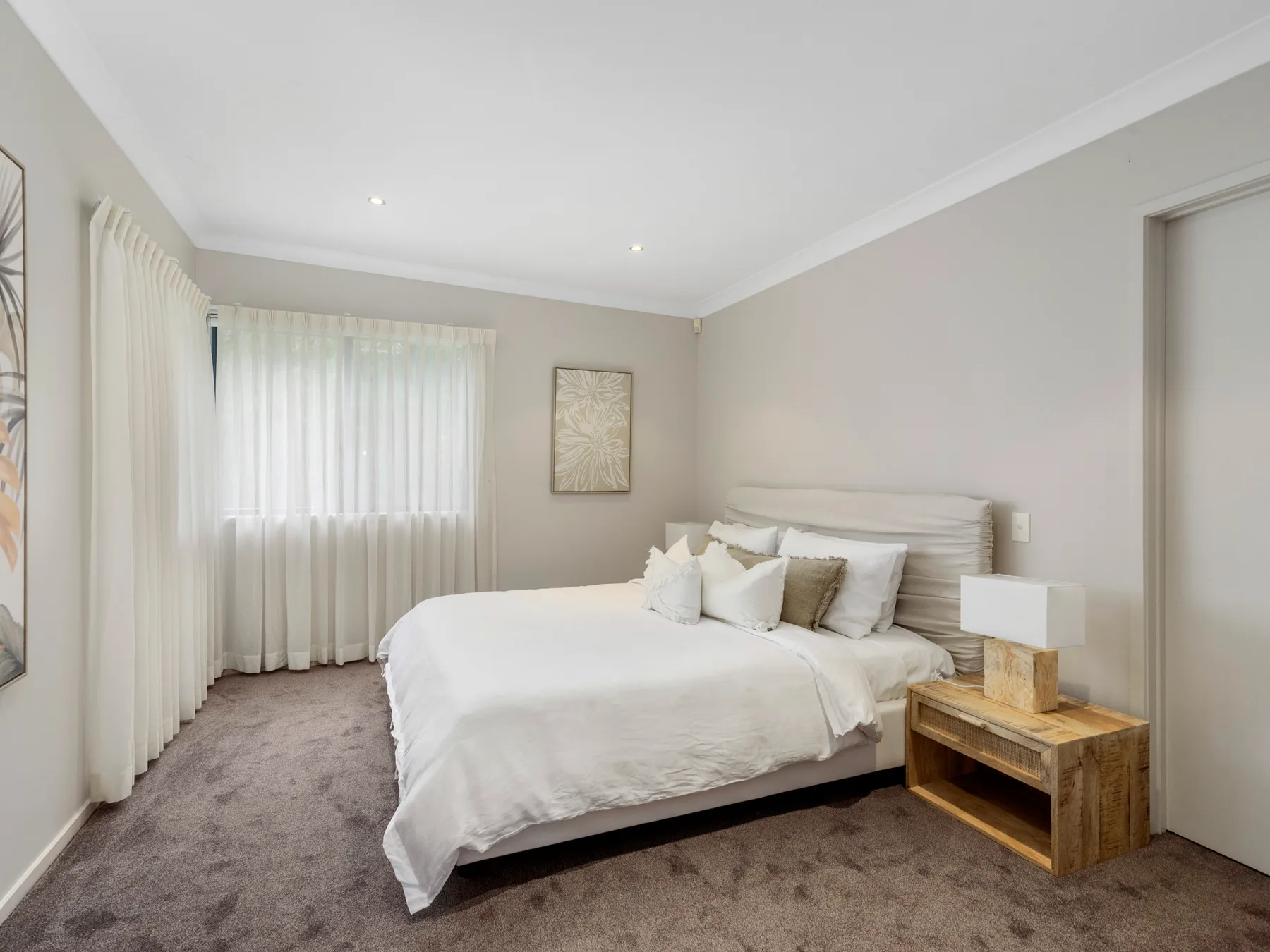 A bright bedroom with a neatly made bed and a curtained window.