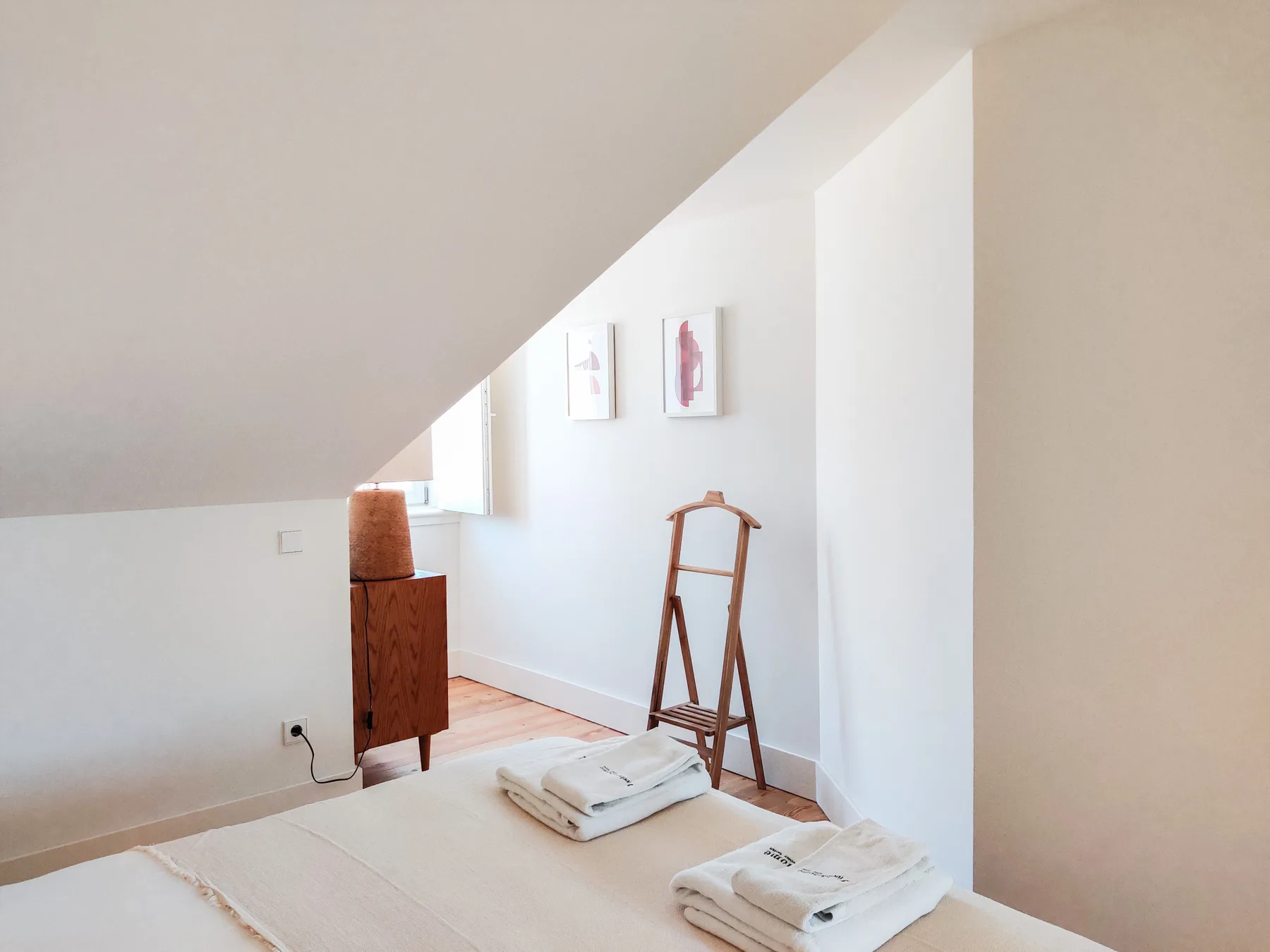 A bright attic bedroom with folded towels on the bed.