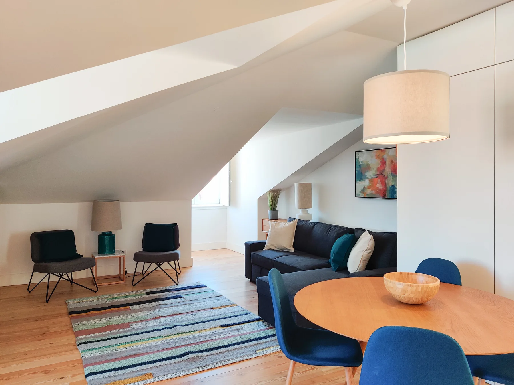 A living area with dark seating, a colorful rug, and a round dining table.