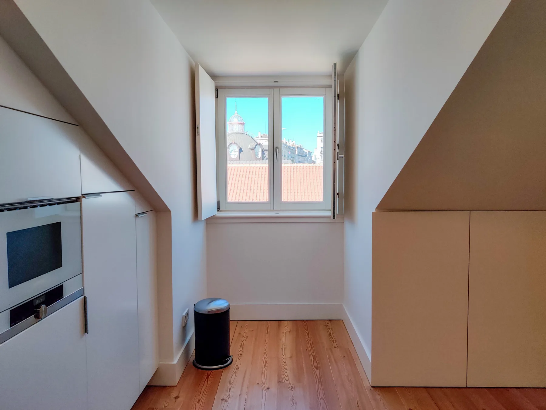 A compact kitchen with built-in appliances and a window overlooking nearby rooftops.