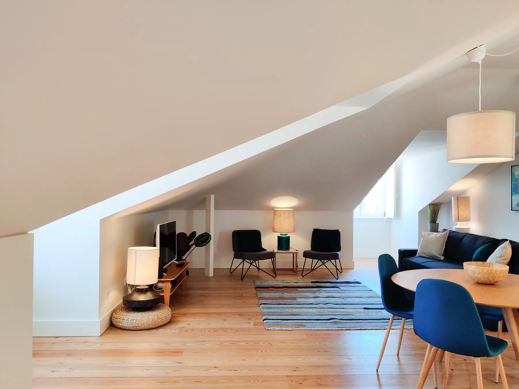 A bright living room with seating, a rug, and a sloped ceiling.