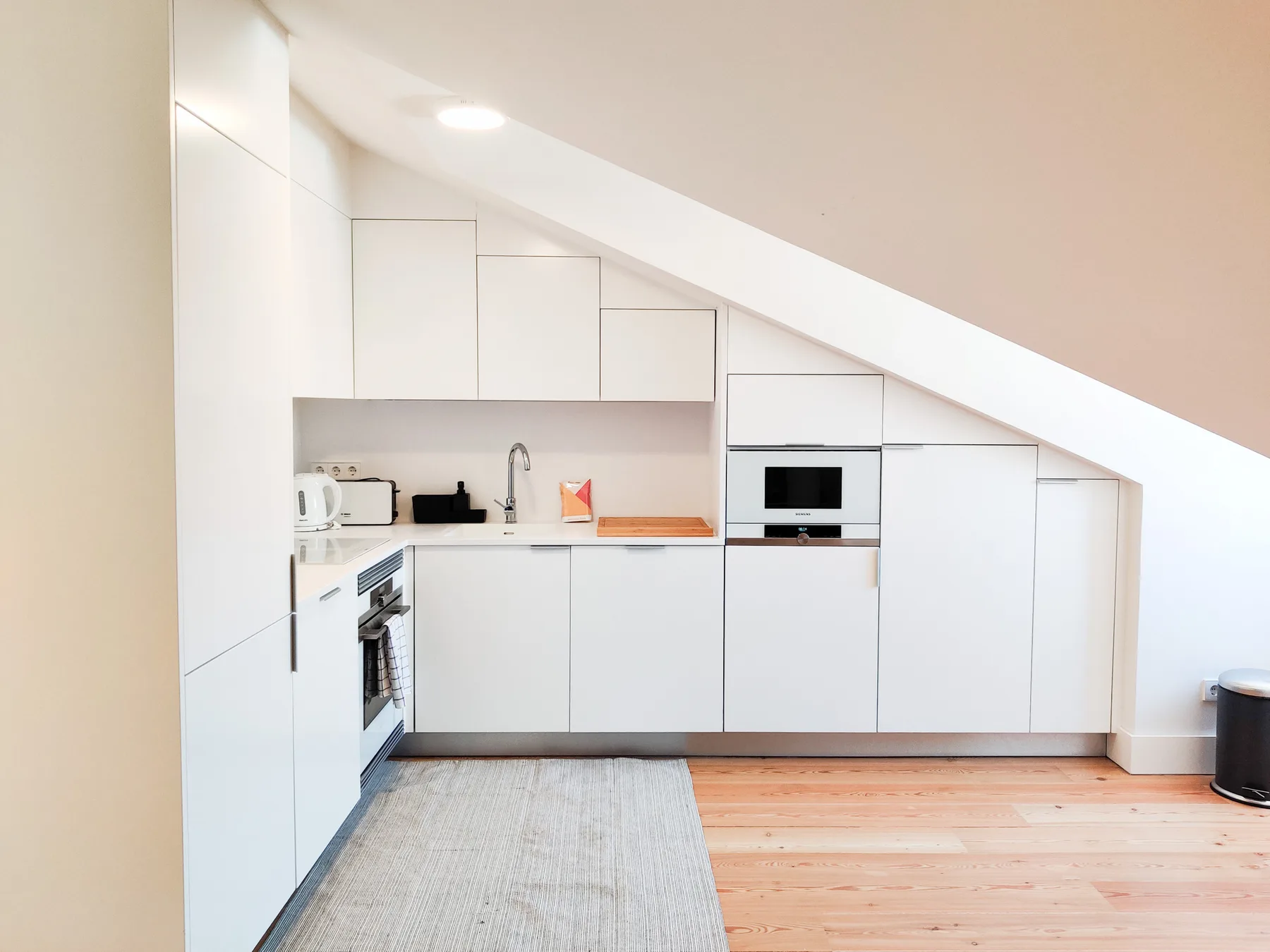 A compact kitchen with white cabinets sits beneath a sloped ceiling.