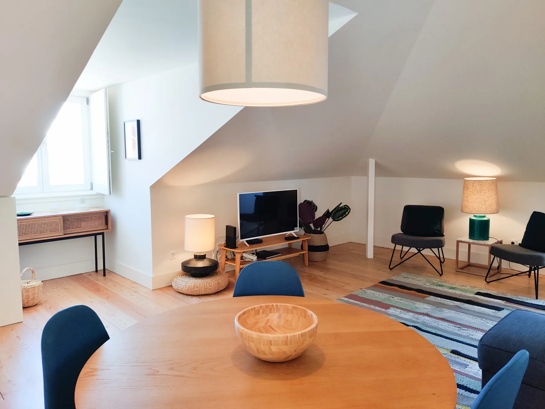 A bright living room with a round wooden table and seating beneath a sloped ceiling.