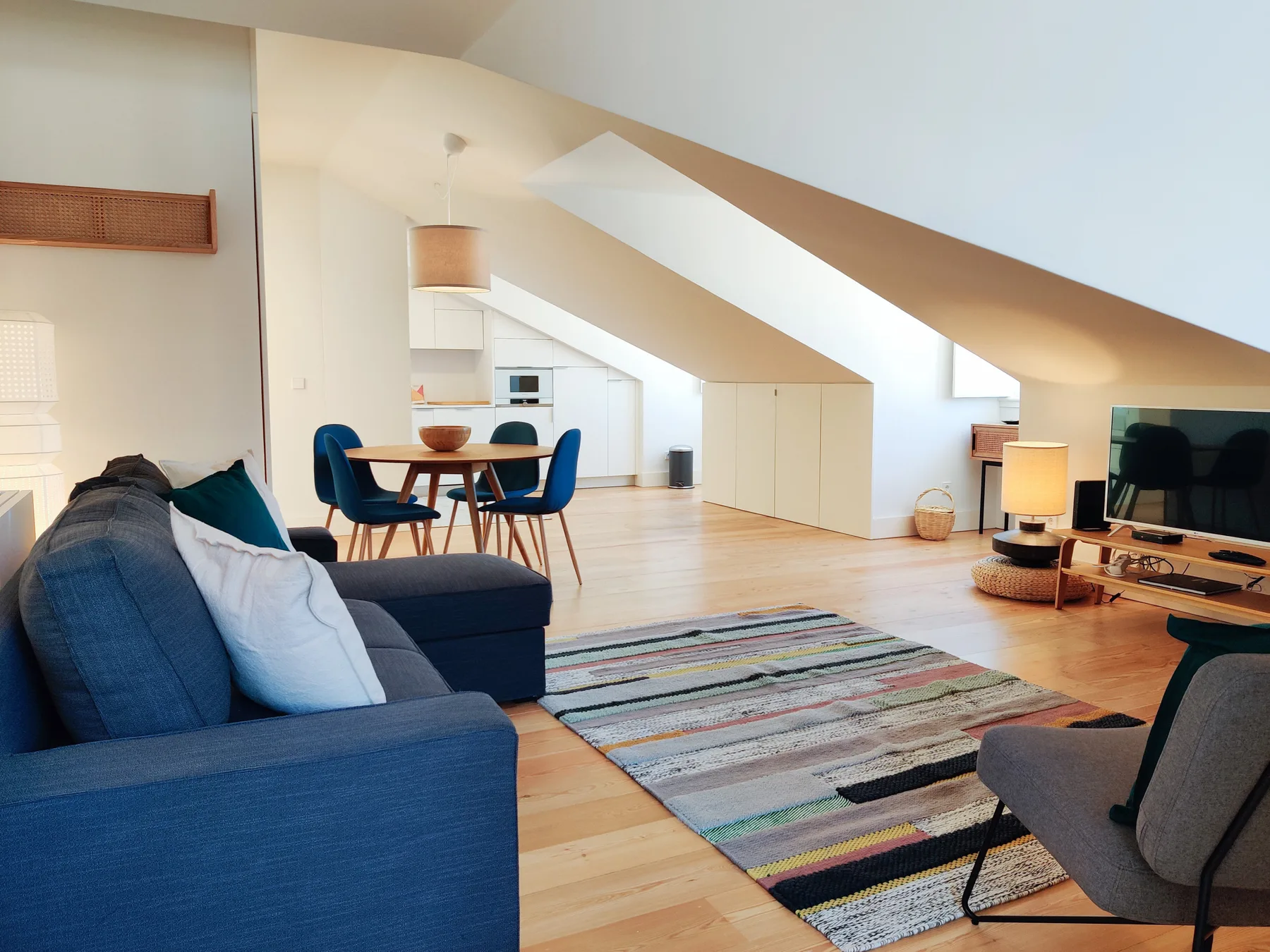 A bright living room with a dining table and seating beneath a sloped ceiling.