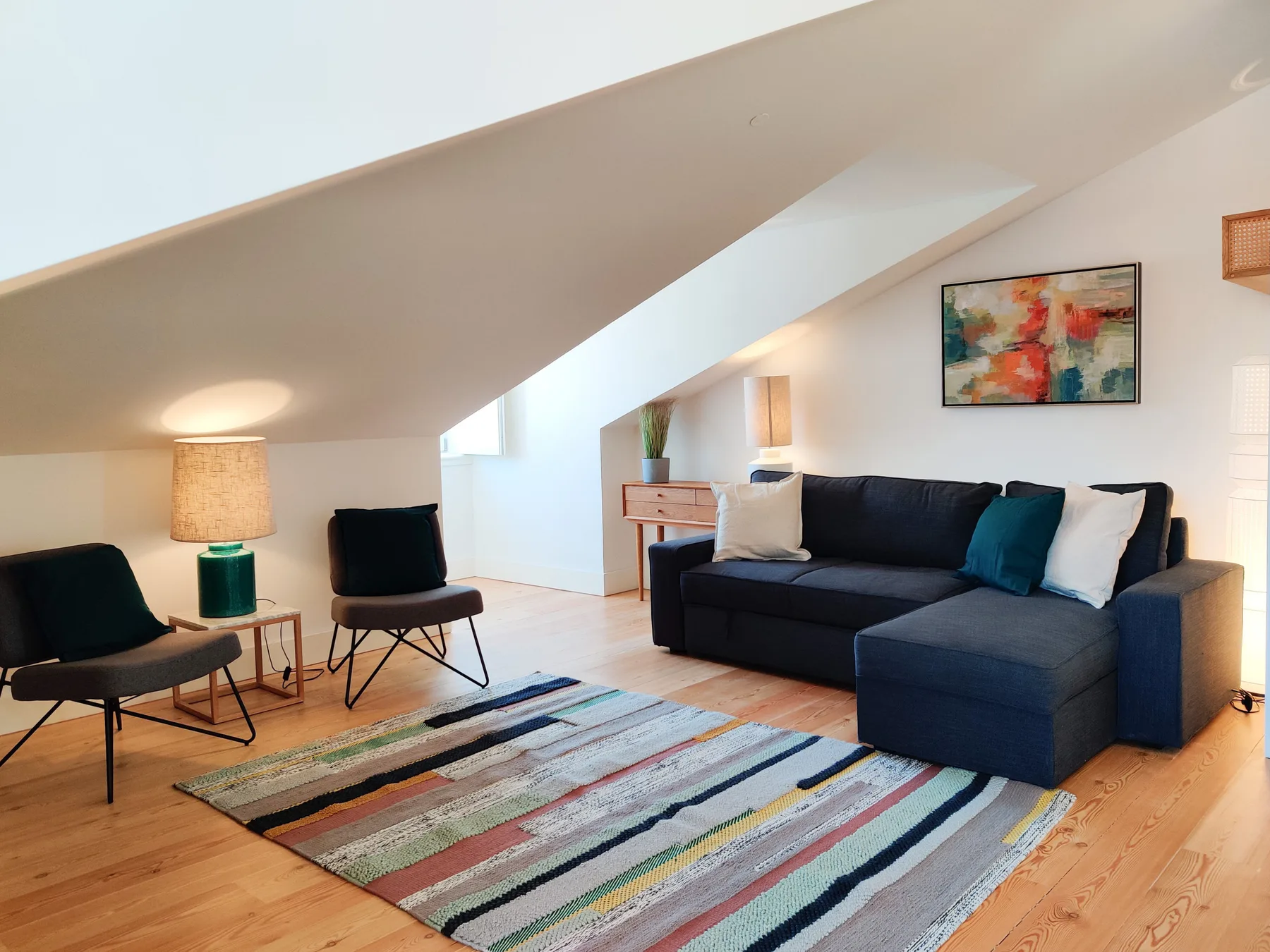 A living room with a dark sectional, colorful rug, and abstract wall art.