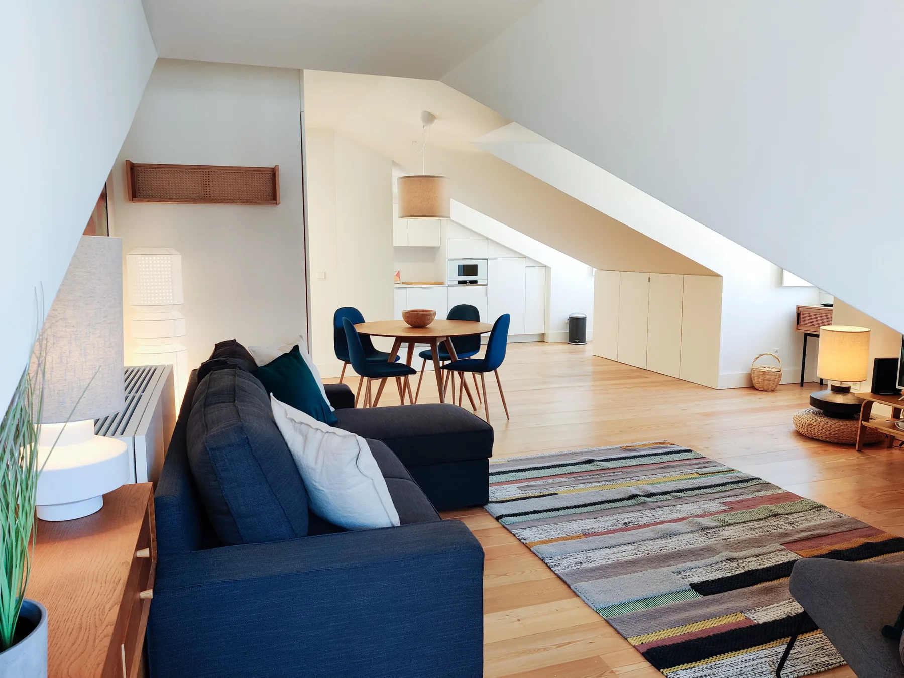 A bright attic living area with seating, a dining table, and a sloped ceiling.