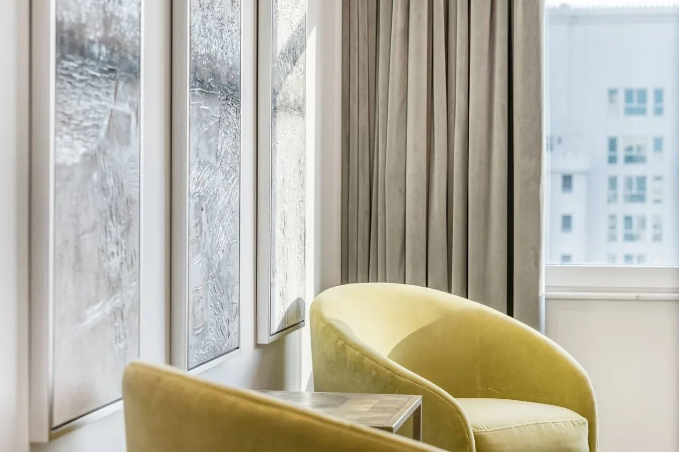A bright seating area with yellow upholstered chairs beside tall windows.