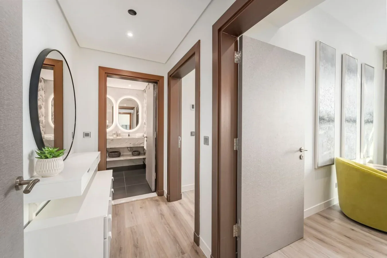 A bright hallway opens toward a bathroom, with a white console and wall mirror.