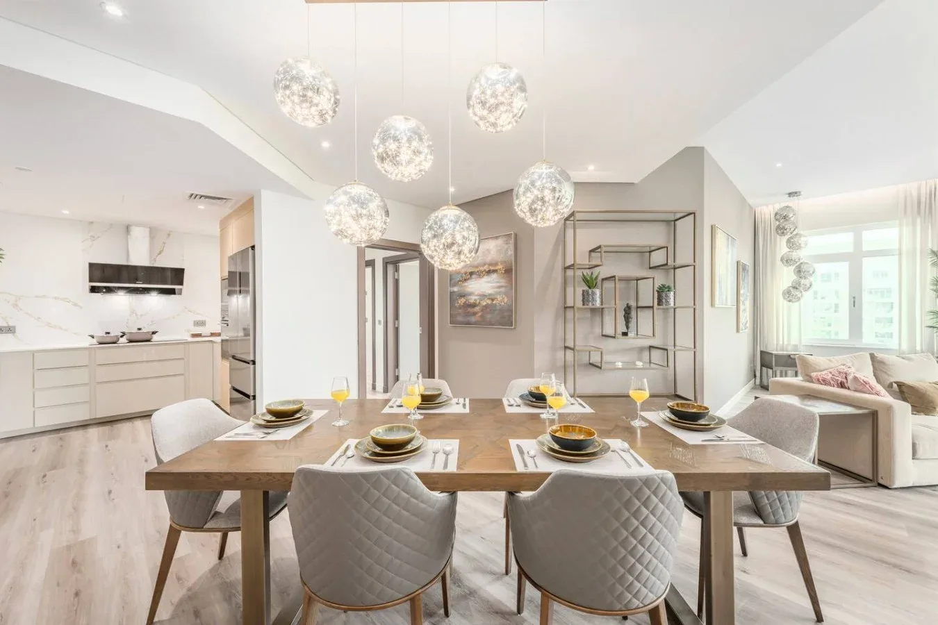 A bright open-plan dining area with a long table and a white kitchen.