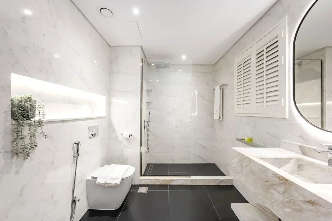 A bright marble bathroom with a walk-in shower and a long vanity.