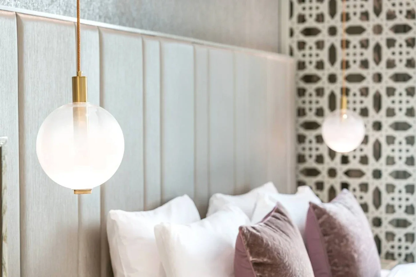 A bedroom with a paneled headboard, pillows, and hanging globe lights.