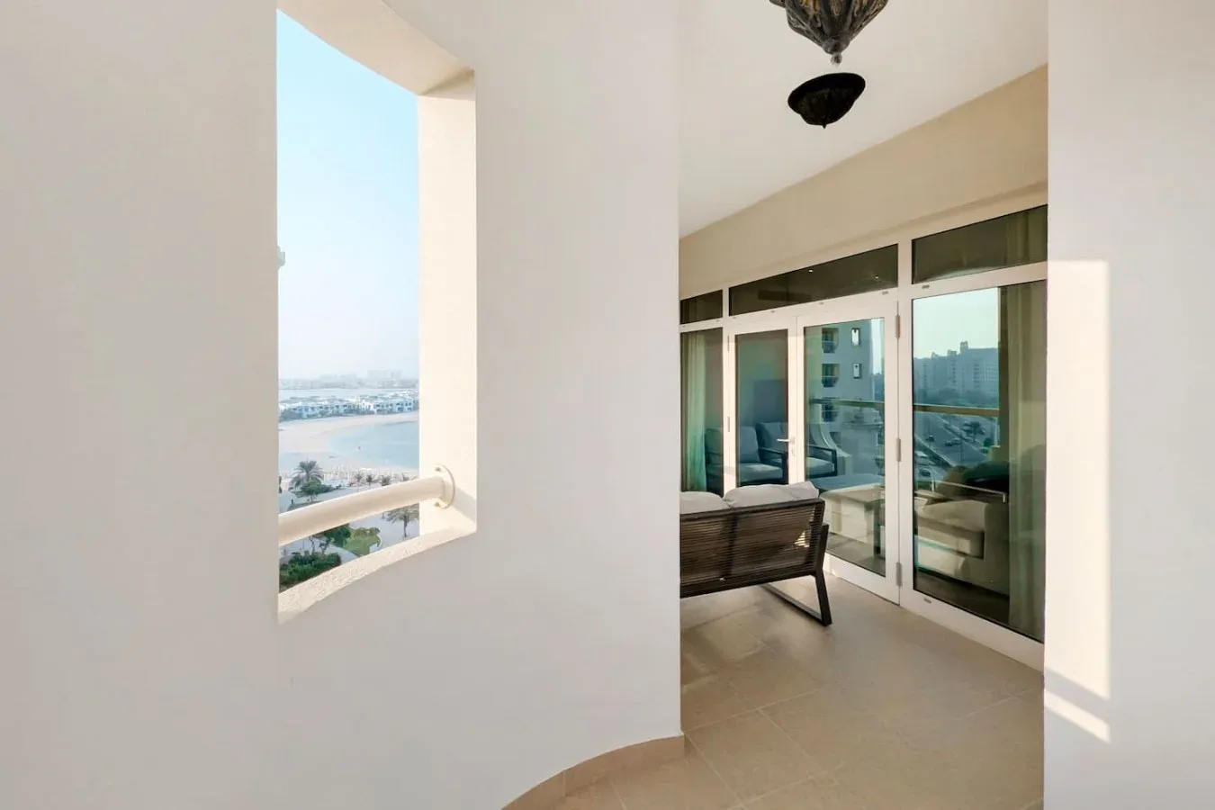 A bright enclosed balcony with a seating area and large windows.