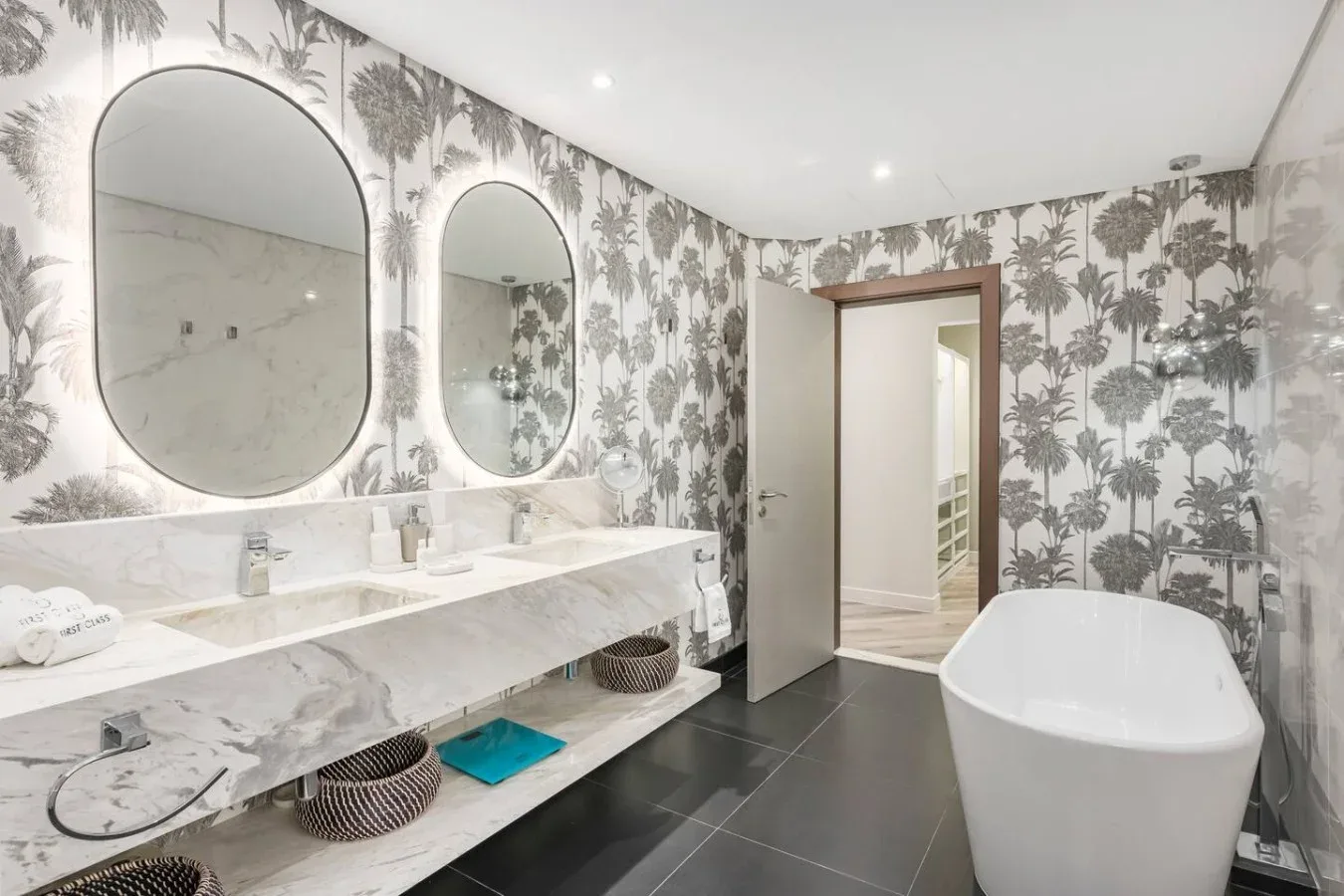 A bathroom with a double vanity, patterned walls, and a freestanding bathtub.