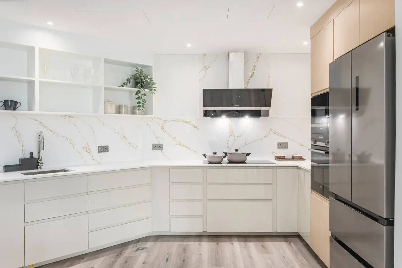 A bright modern kitchen with white cabinetry, open shelving, and a stainless steel refrigerator.