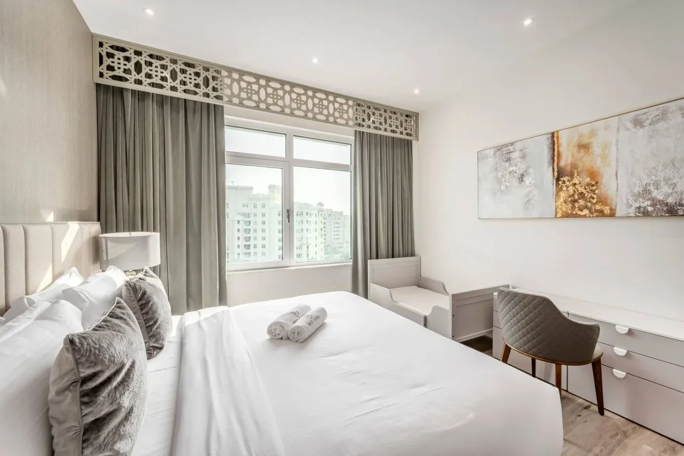 A bright bedroom with a large bed, a window, and a small seating area.