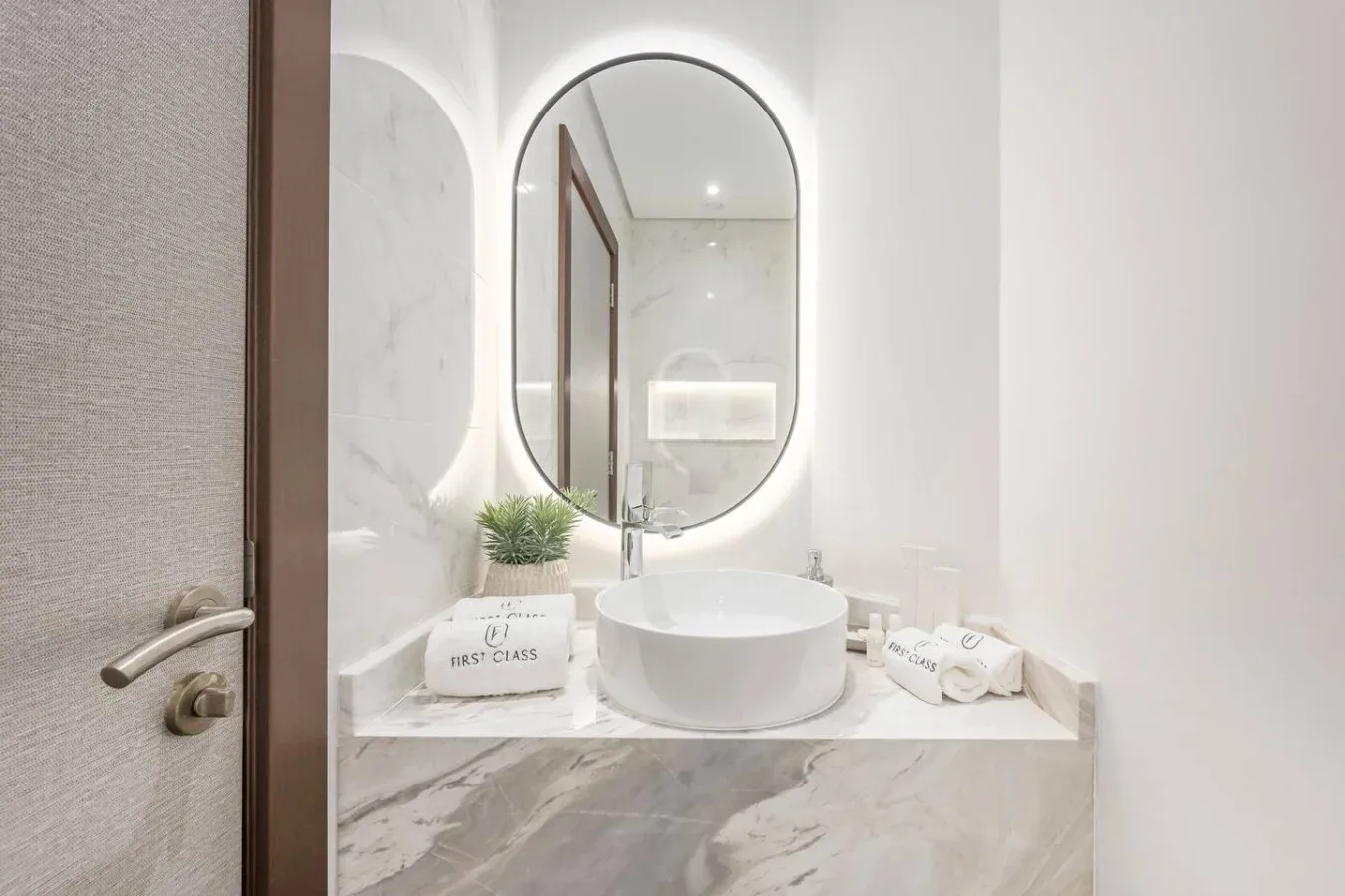 A bright bathroom vanity features a round vessel sink beneath an oval mirror.