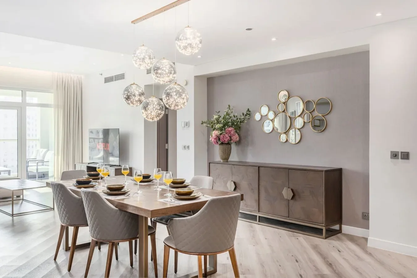 A dining area with a long table, upholstered seating, and pendant lights.