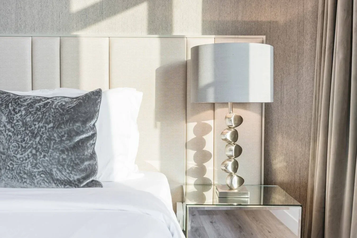A bedroom with a neatly made bed and a bedside lamp.