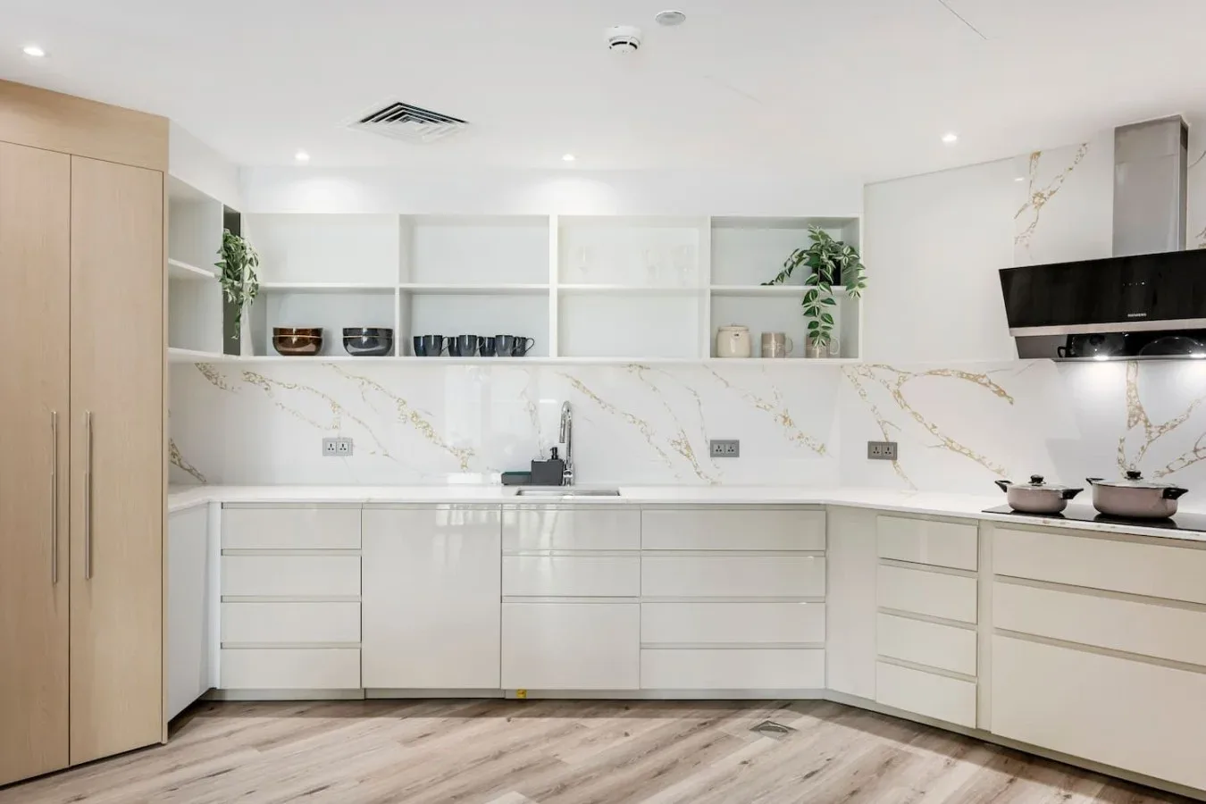A bright modern kitchen with white cabinetry, open shelves, and a countertop.