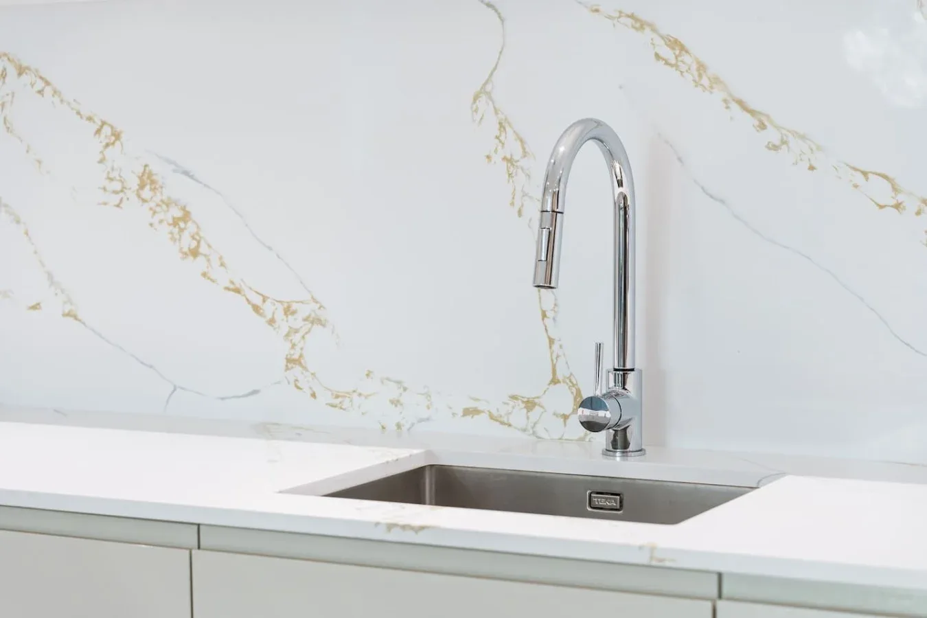 A kitchen sink with a curved faucet sits against a veined white backsplash.