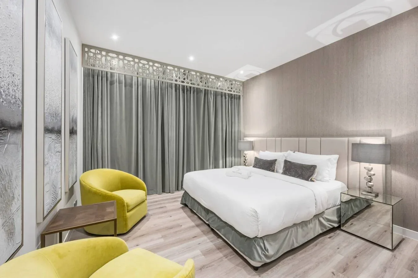 A bedroom with a neatly made bed, gray curtains, and a yellow armchair.