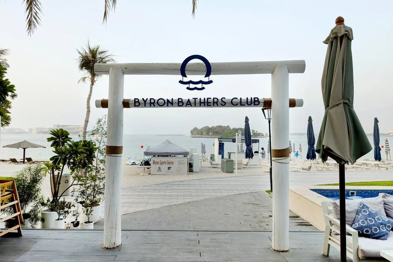 A beach club entrance opens onto a seaside deck with loungers and umbrellas.